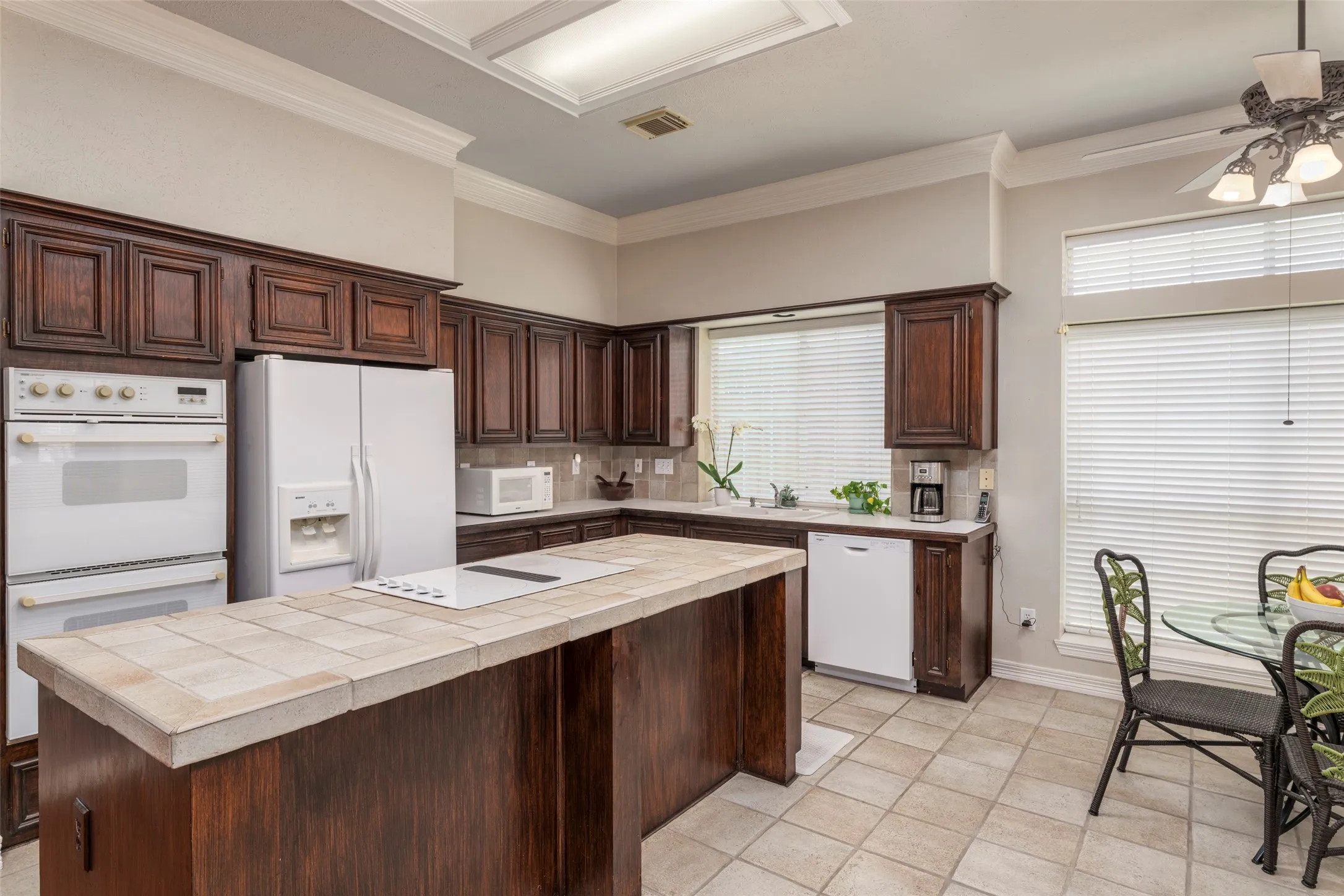 Kitchen featuring wood cabinetry, a center island with tile countertop, tile flooring, and integrated double ovens