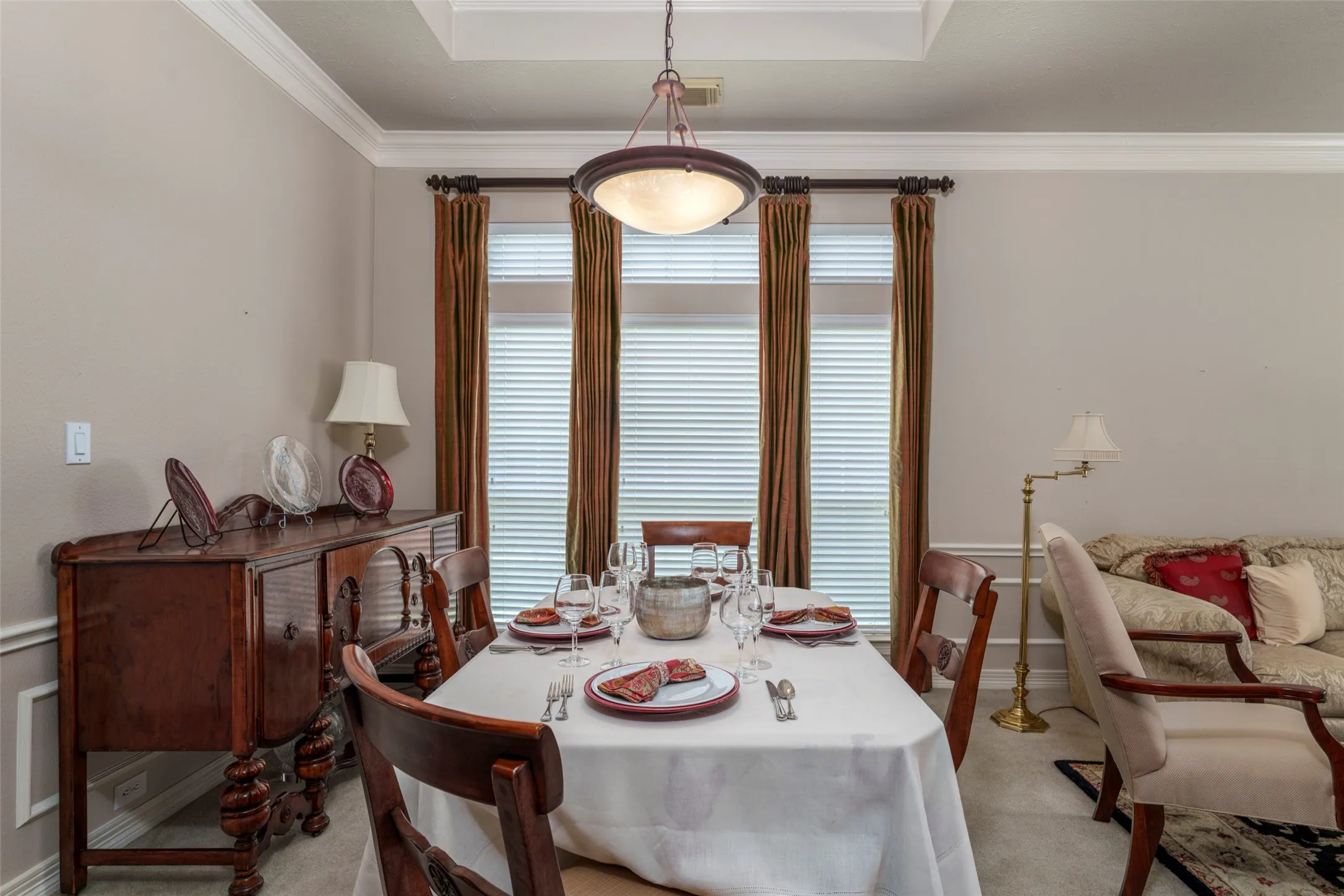 Recessed ceiling with crown molding, tray ceiling detail, three windows with blinds, and an integrated ceiling light fixture