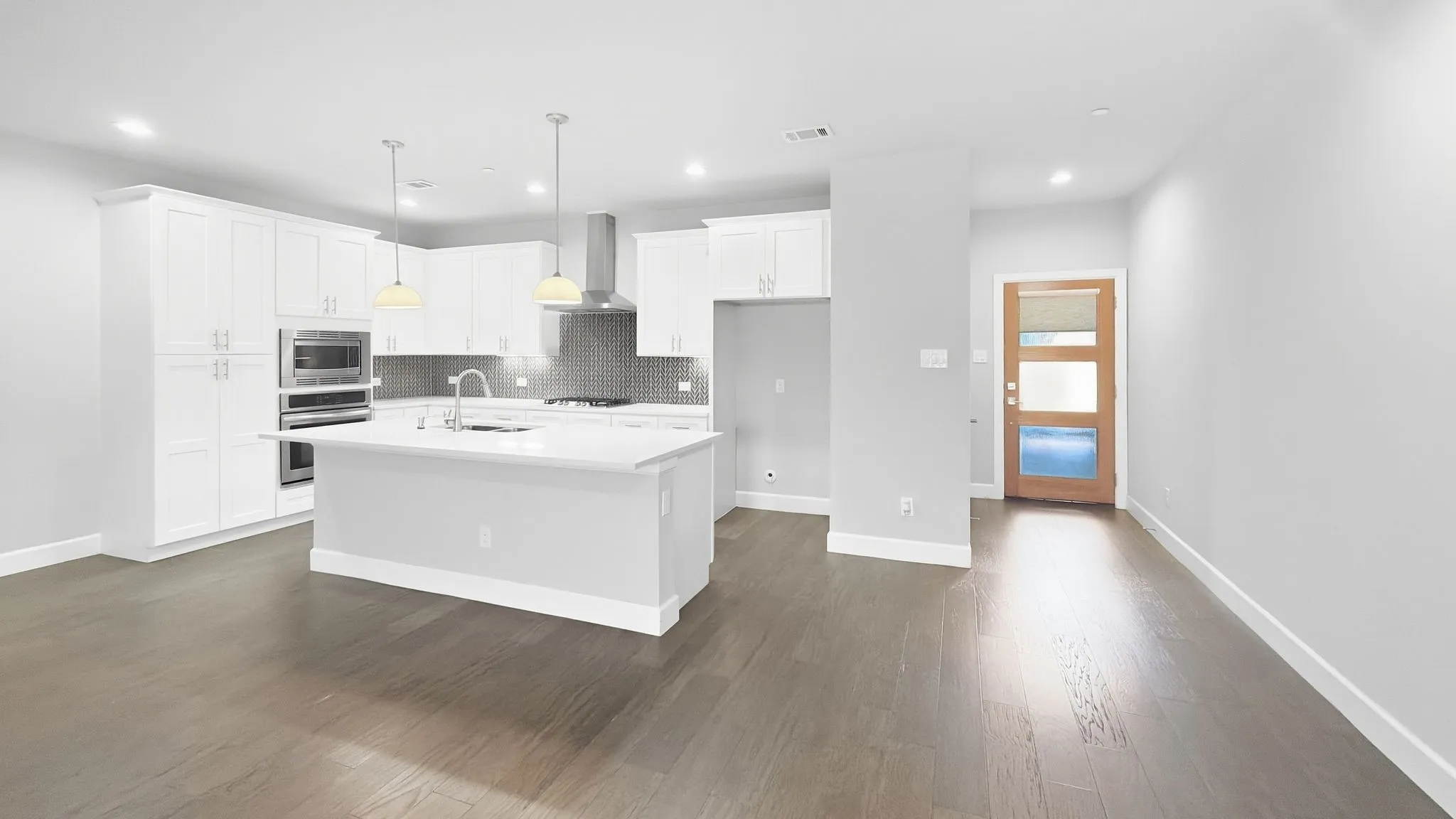 Kitchen featuring white cabinetry, stainless steel appliances, a center island with sink, pendant lighting, and wood-finish flooring