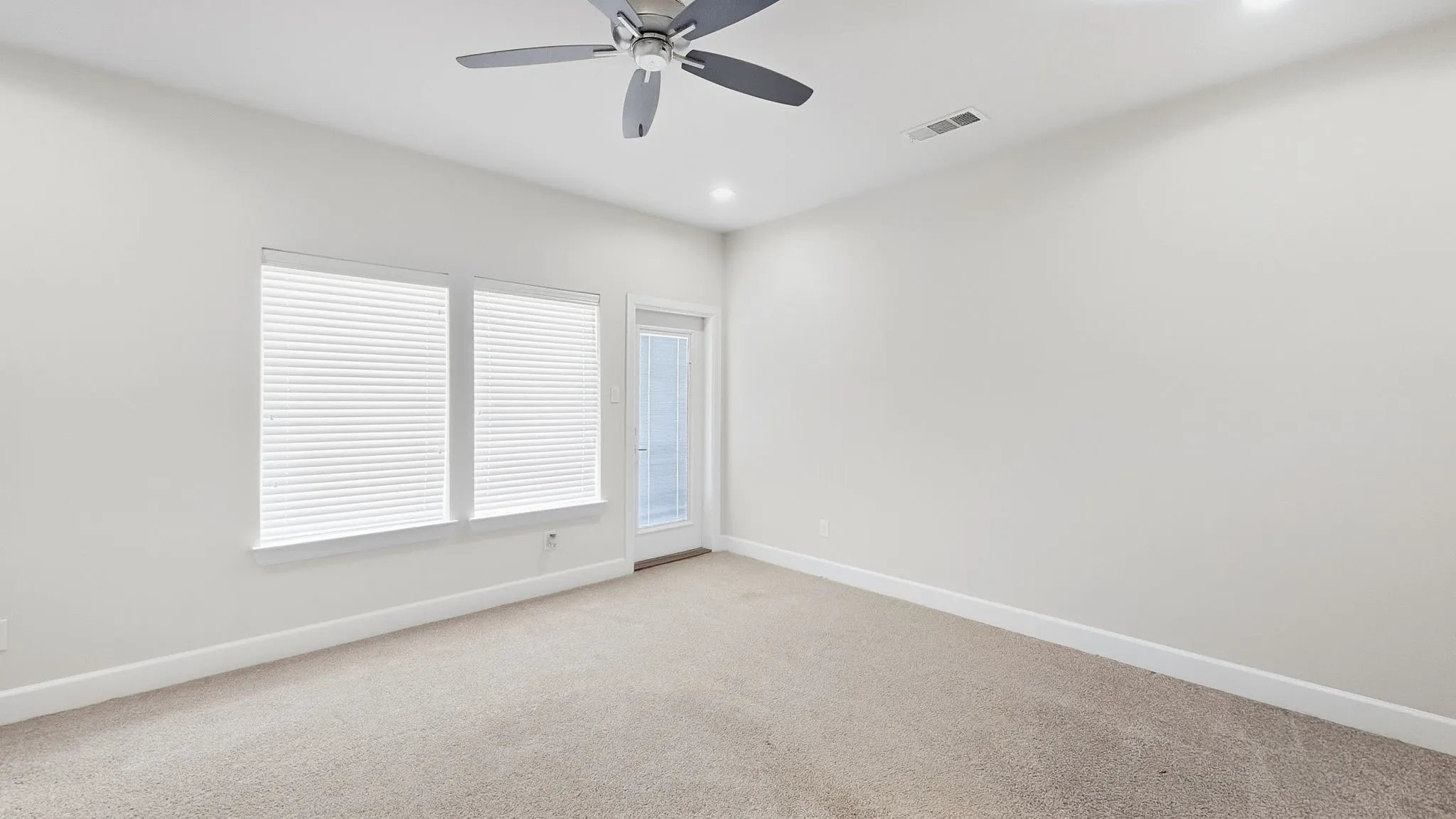 Carpeted flooring, recessed lighting, ceiling fan, two windows with blinds, and an exterior door