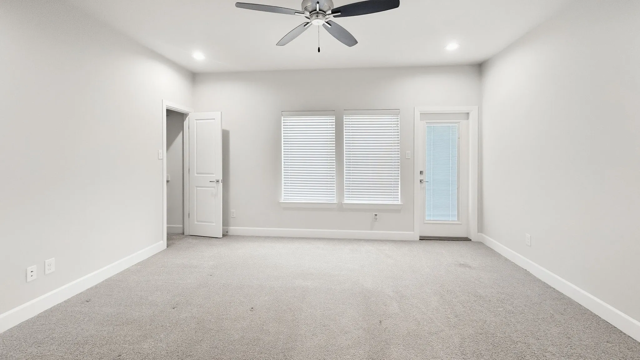 Recessed lighting, ceiling fan, carpeting, two windows with blinds, and an exterior door