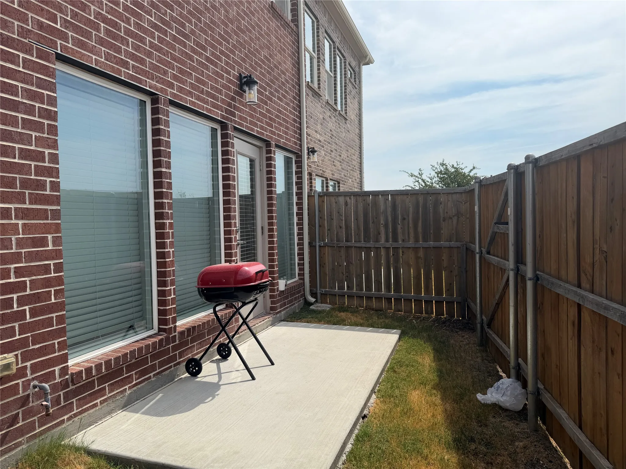 Brick exterior with a concrete patio, wood privacy fencing, and two large windows