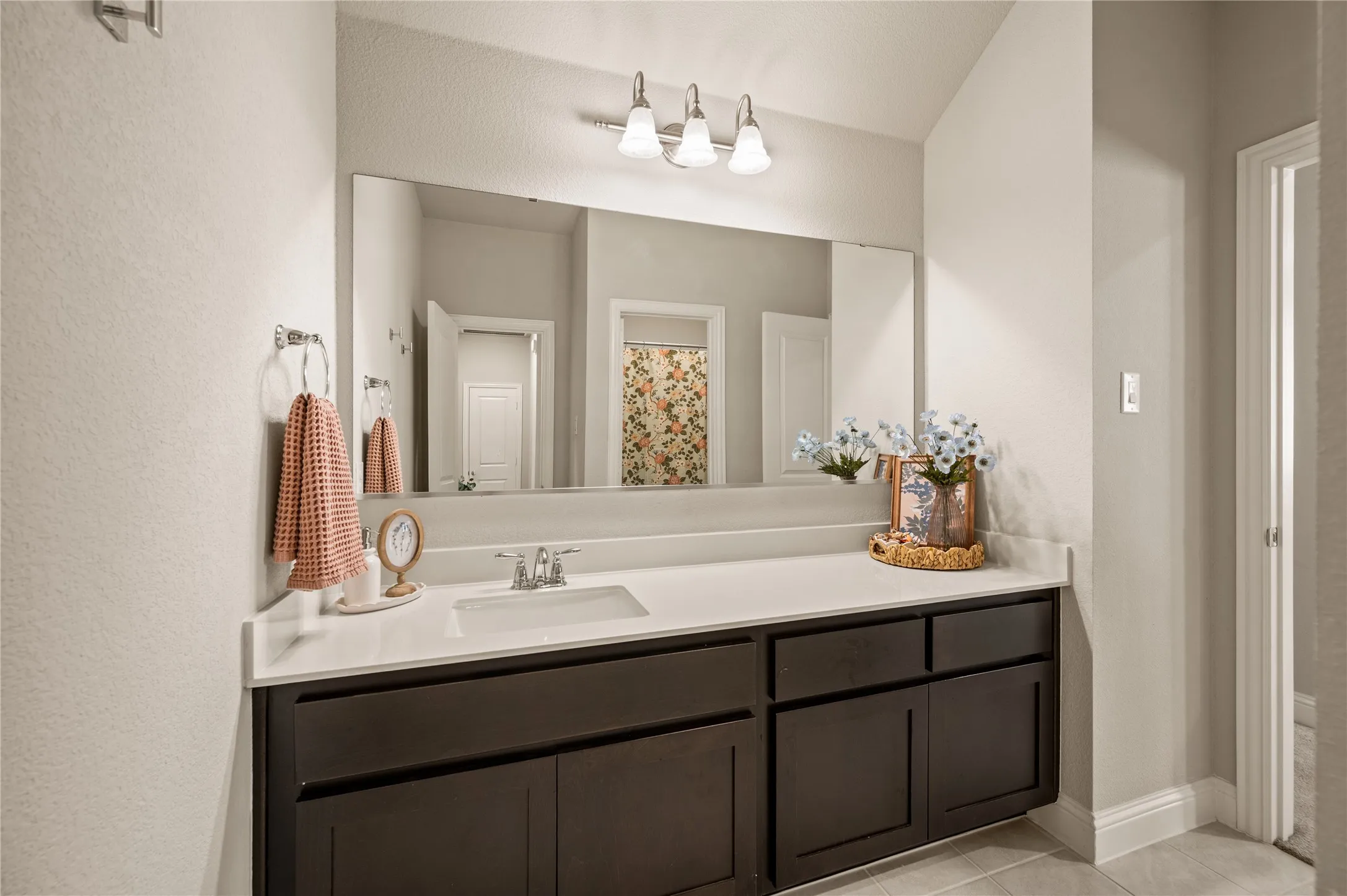 Vanity with dark wood-finish cabinetry, integrated sink, and light-toned countertop, complemented by a large wall-mounted mirror and brushed nickel vanity lighting