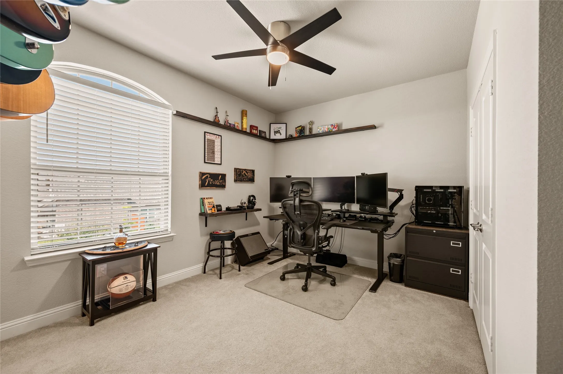 Carpeted room featuring a ceiling fan with integrated lighting, a multi-pane arched window, and built-in shelving
