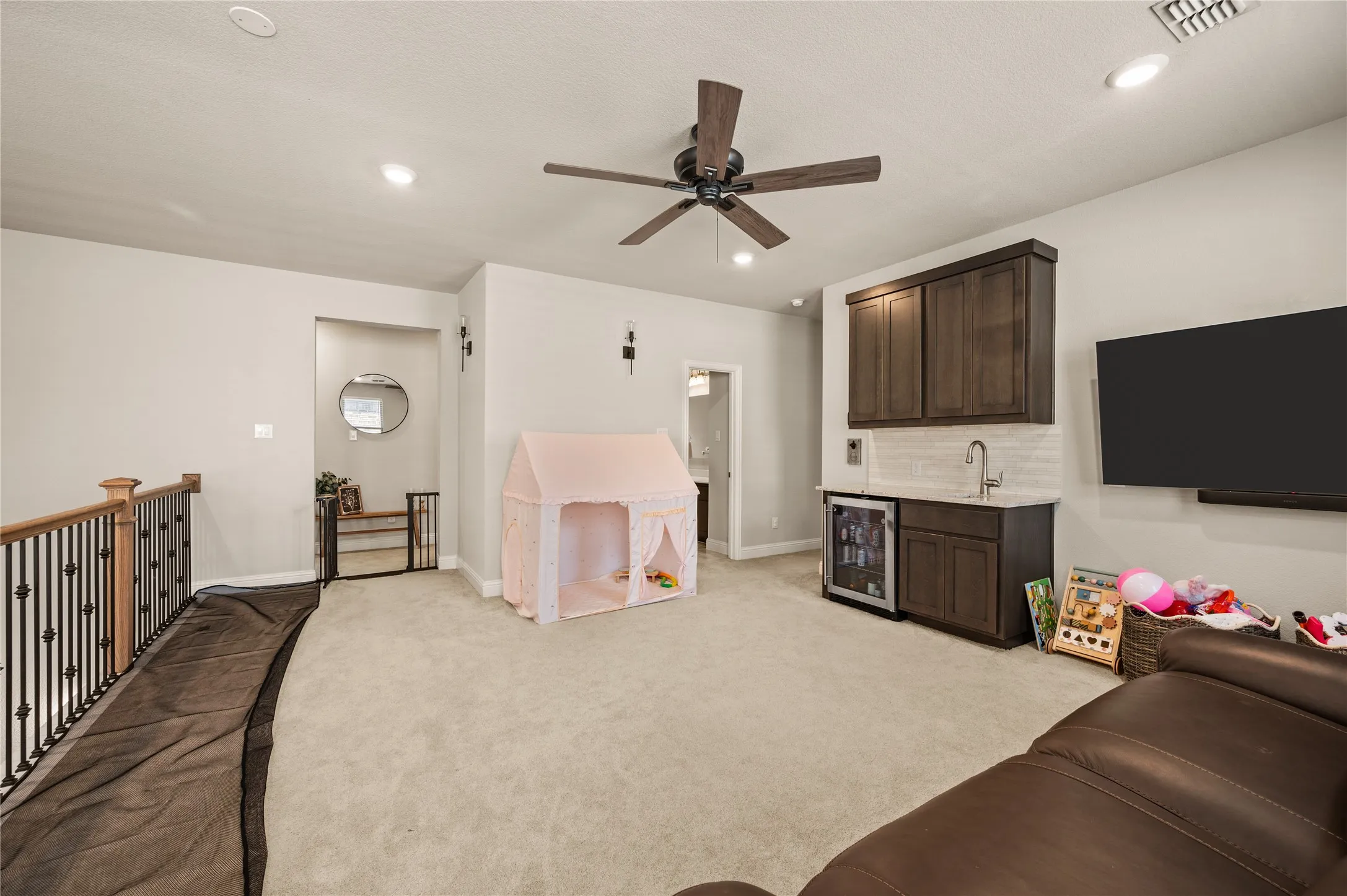 Carpeted room featuring a ceiling fan, recessed lighting, and a built-in wet bar with dark wood-finish cabinetry, a beverage refrigerator, and a stainless steel sink