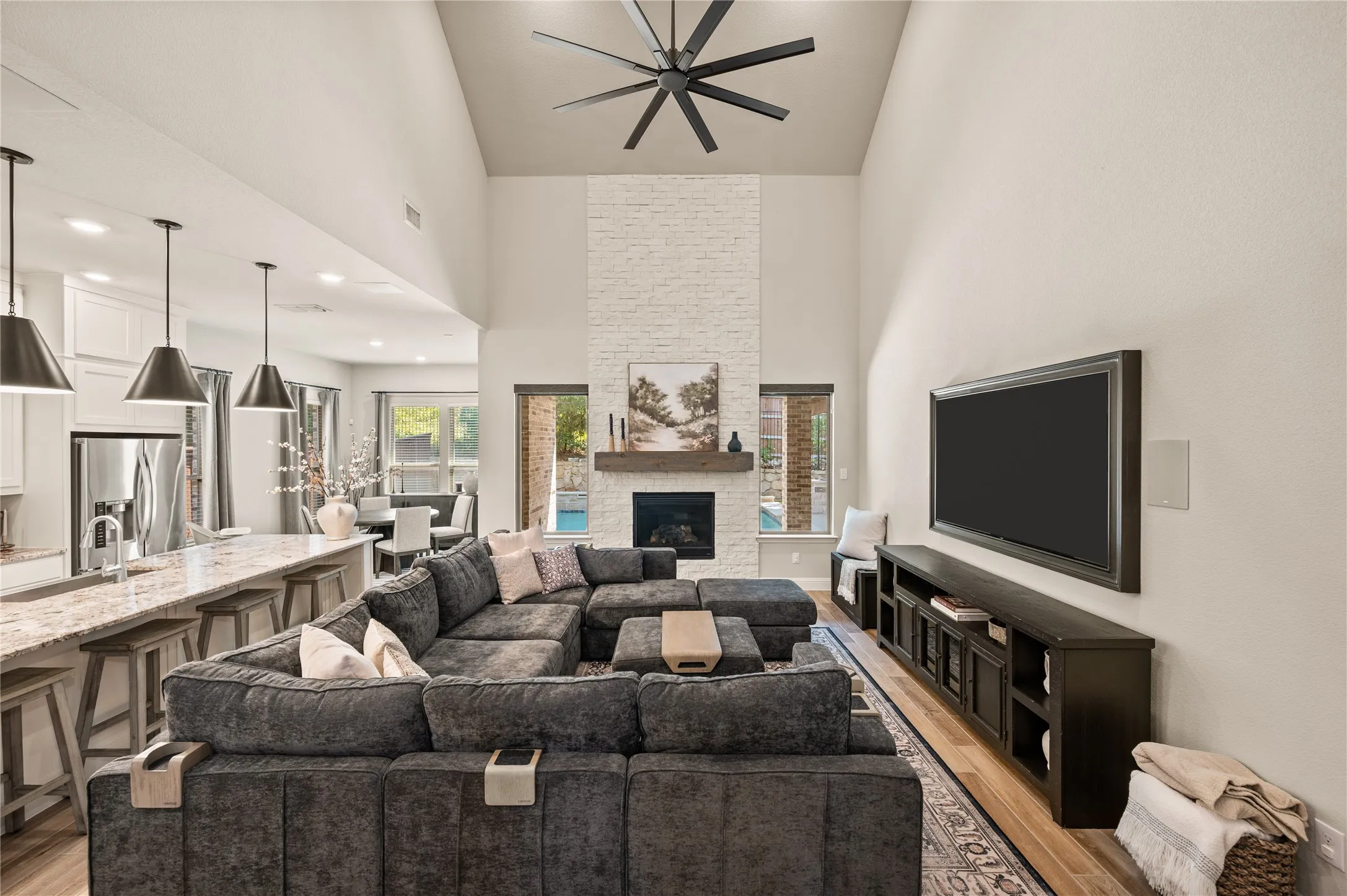 Vaulted ceilings, wood-finish flooring, a contemporary ceiling fan, and a fireplace with a white brick surround