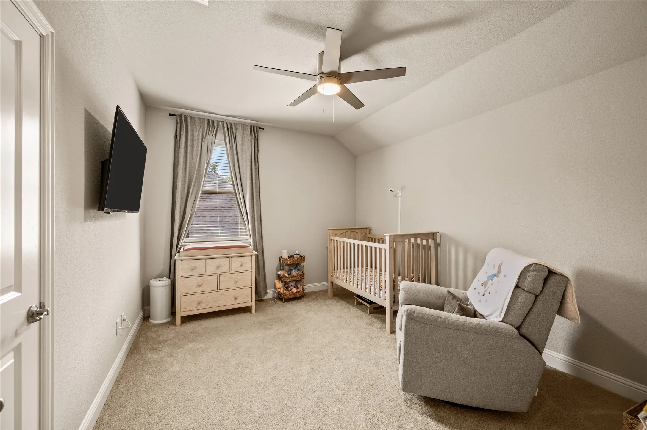 Vaulted ceiling with a contemporary ceiling fan, neutral wall tones, carpeted flooring, and a window with blinds and drapes