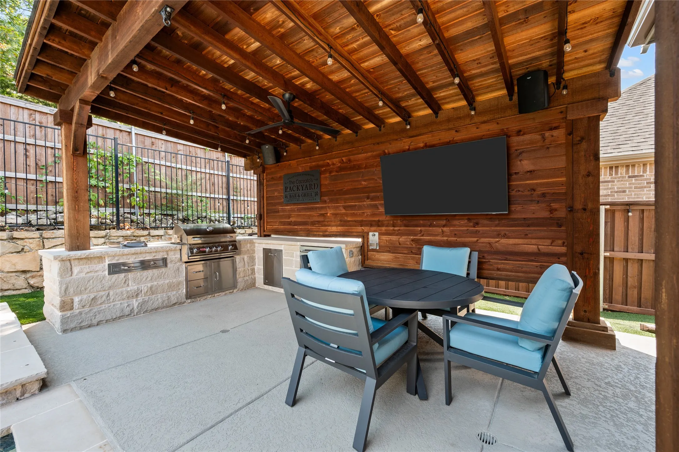Outdoor covered patio with a wood-plank ceiling, wood-paneled accent wall, and built-in outdoor kitchen featuring a grill
