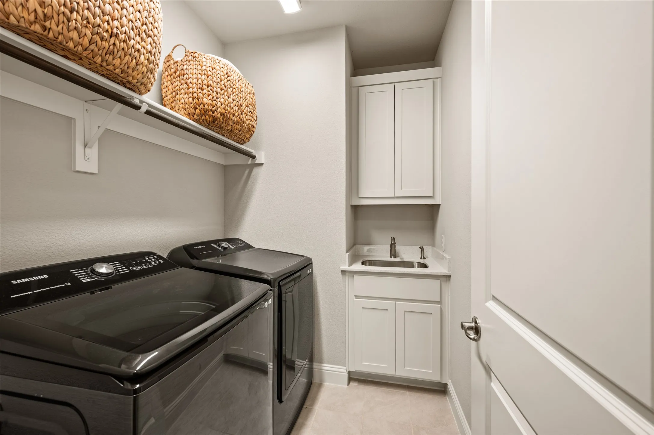 Laundry area featuring a utility sink with a stainless steel faucet, built-in white cabinetry, and an overhead shelf with a hanging rod