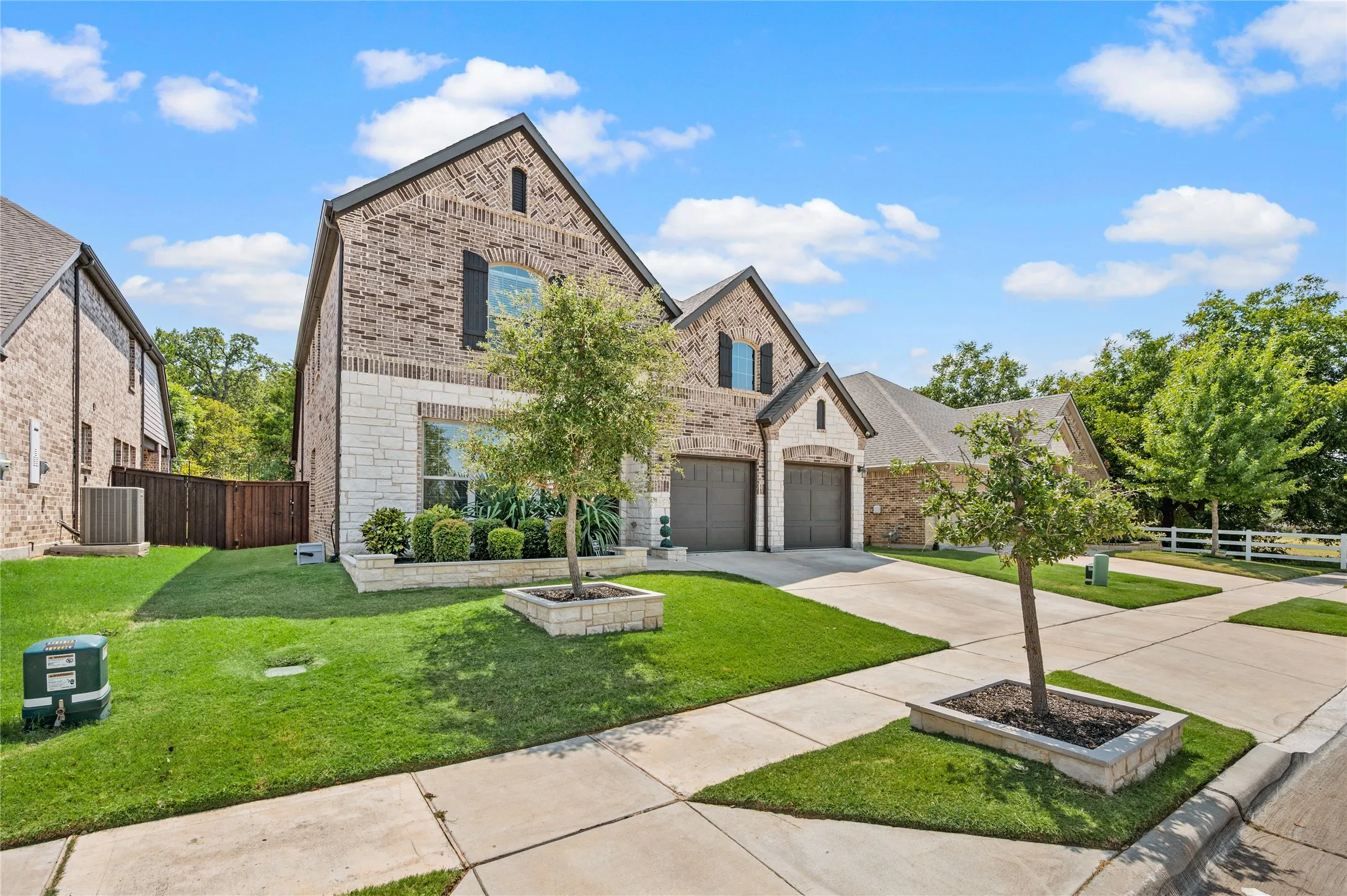 Brick and stone exterior with architectural shingles, attached two-car garage, and manicured landscaping
