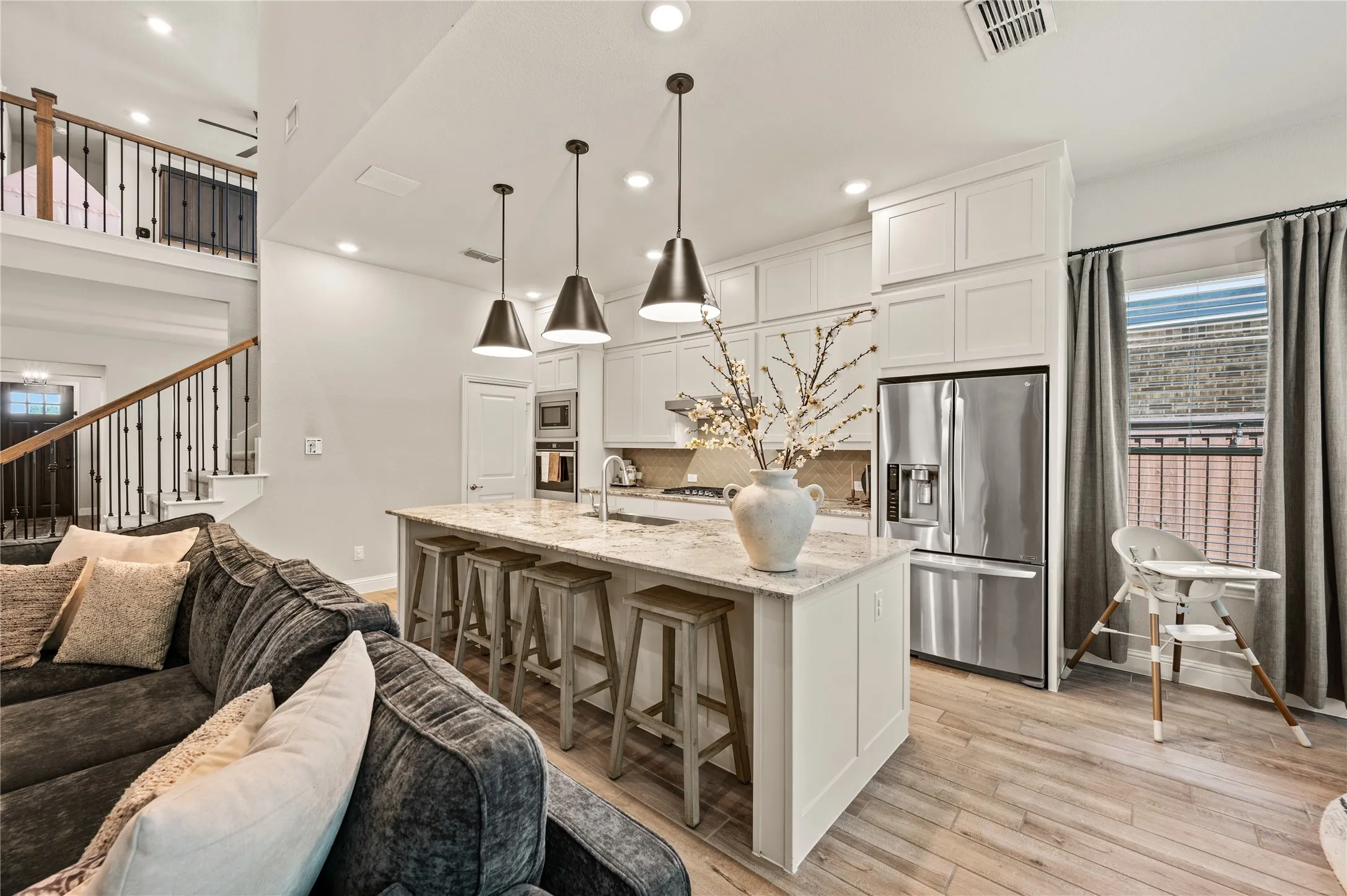 Open-concept living area featuring a kitchen island with seating, pendant lighting, stainless steel appliances, and wood-finish flooring