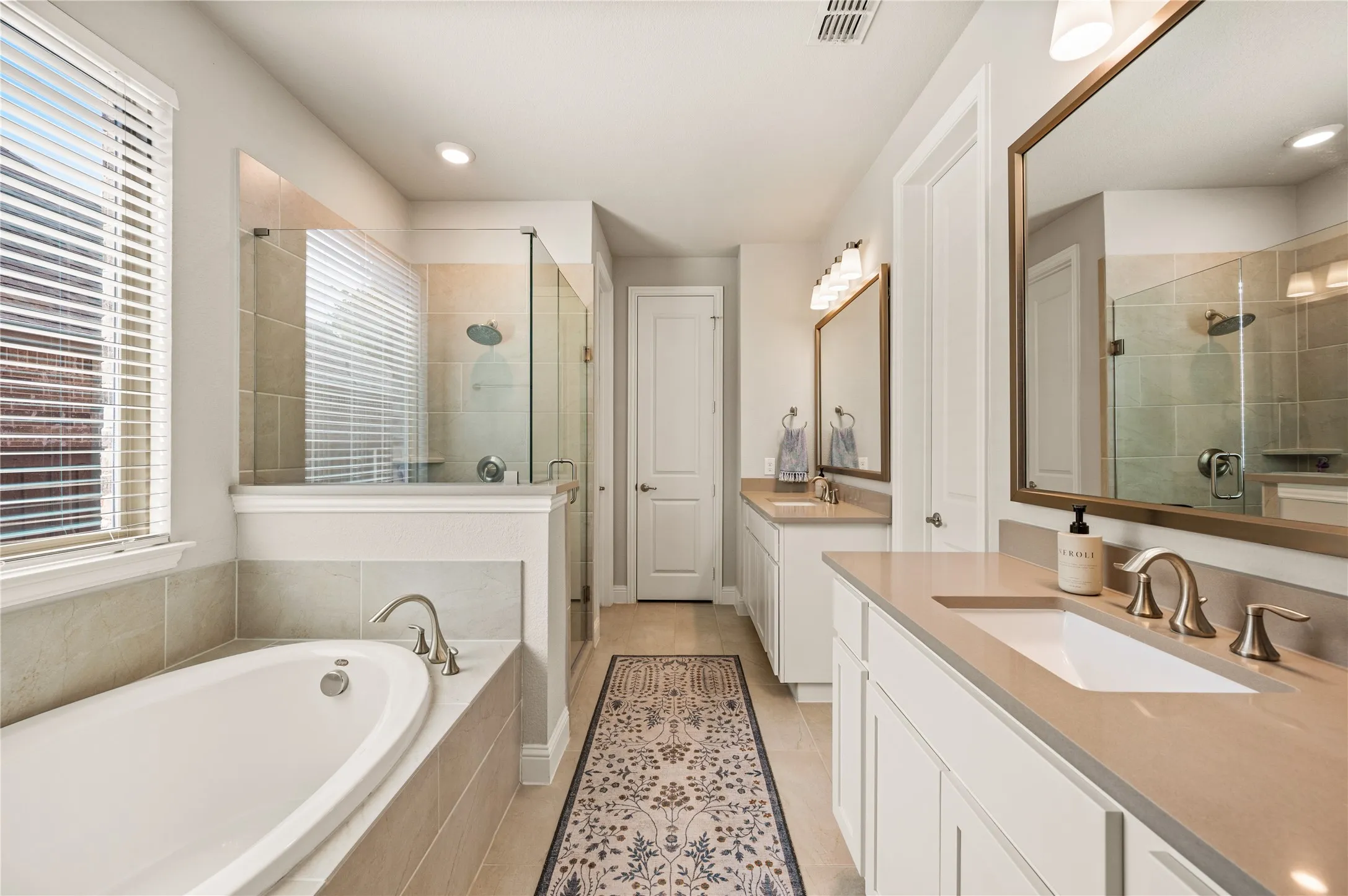 Dual vanity sinks with neutral countertops, a large soaking tub, a separate glass-enclosed shower, and recessed lighting
