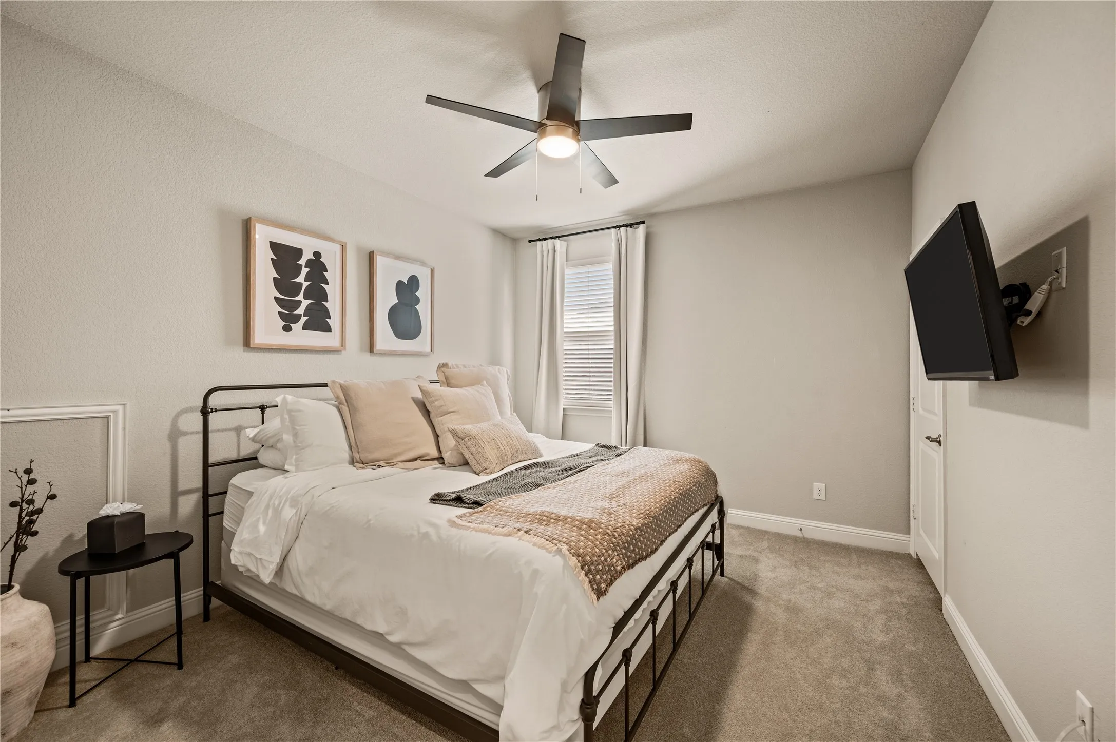 Carpeted bedroom featuring a ceiling fan with integrated lighting, a window with blinds and drapes, and a wall-mounted television bracket