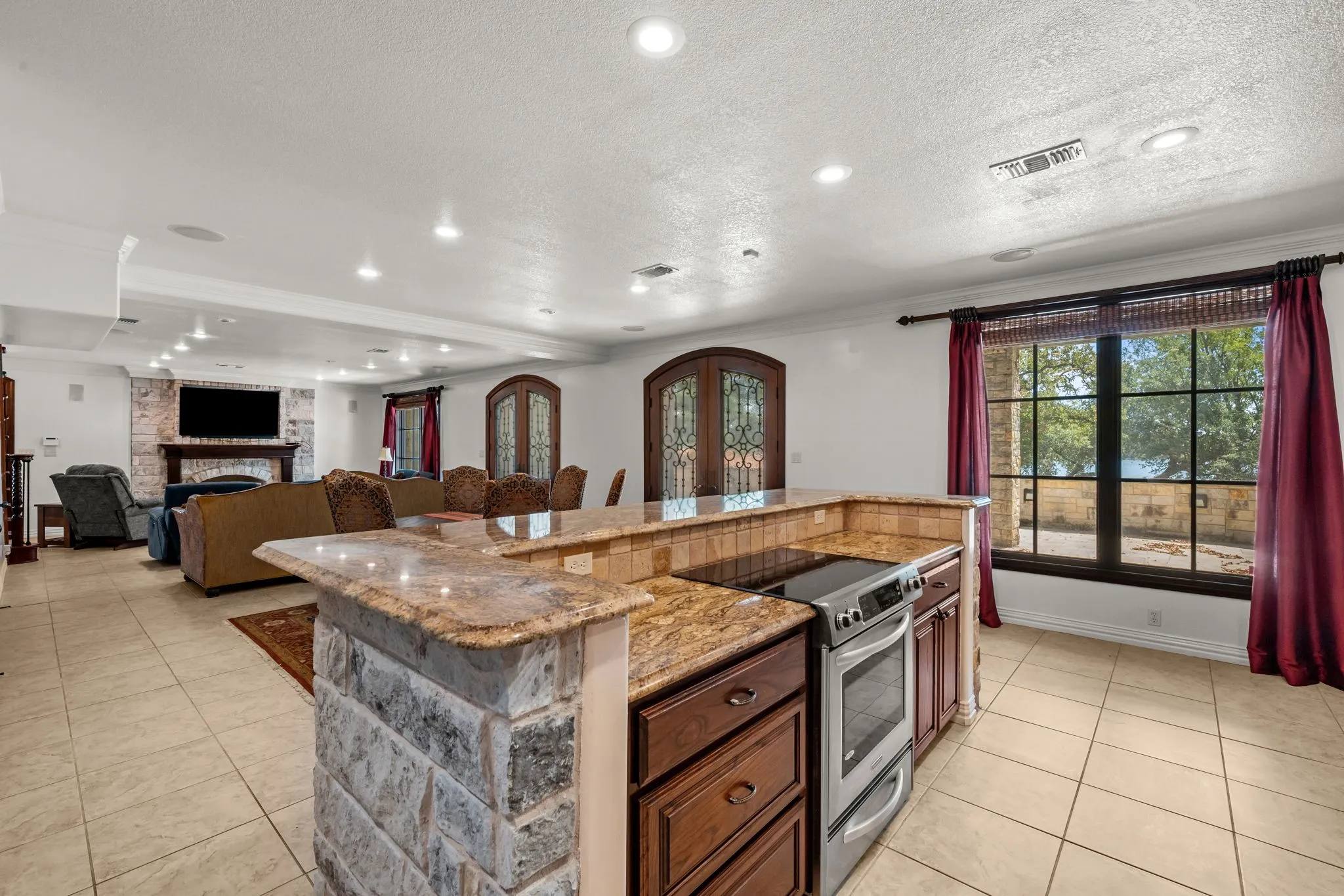 Spacious room featuring a stone-clad kitchen island with granite countertops, rich wood cabinetry, stainless steel appliances, and tile flooring