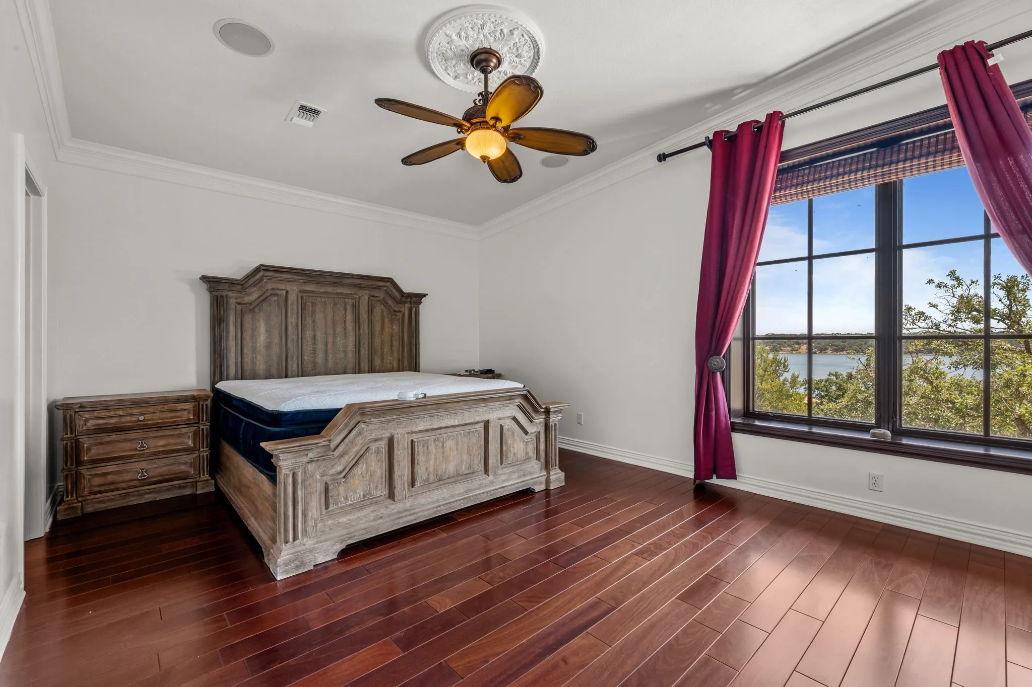 Hardwood flooring, crown molding, ceiling fan with decorative medallion, and expansive window with water scenery