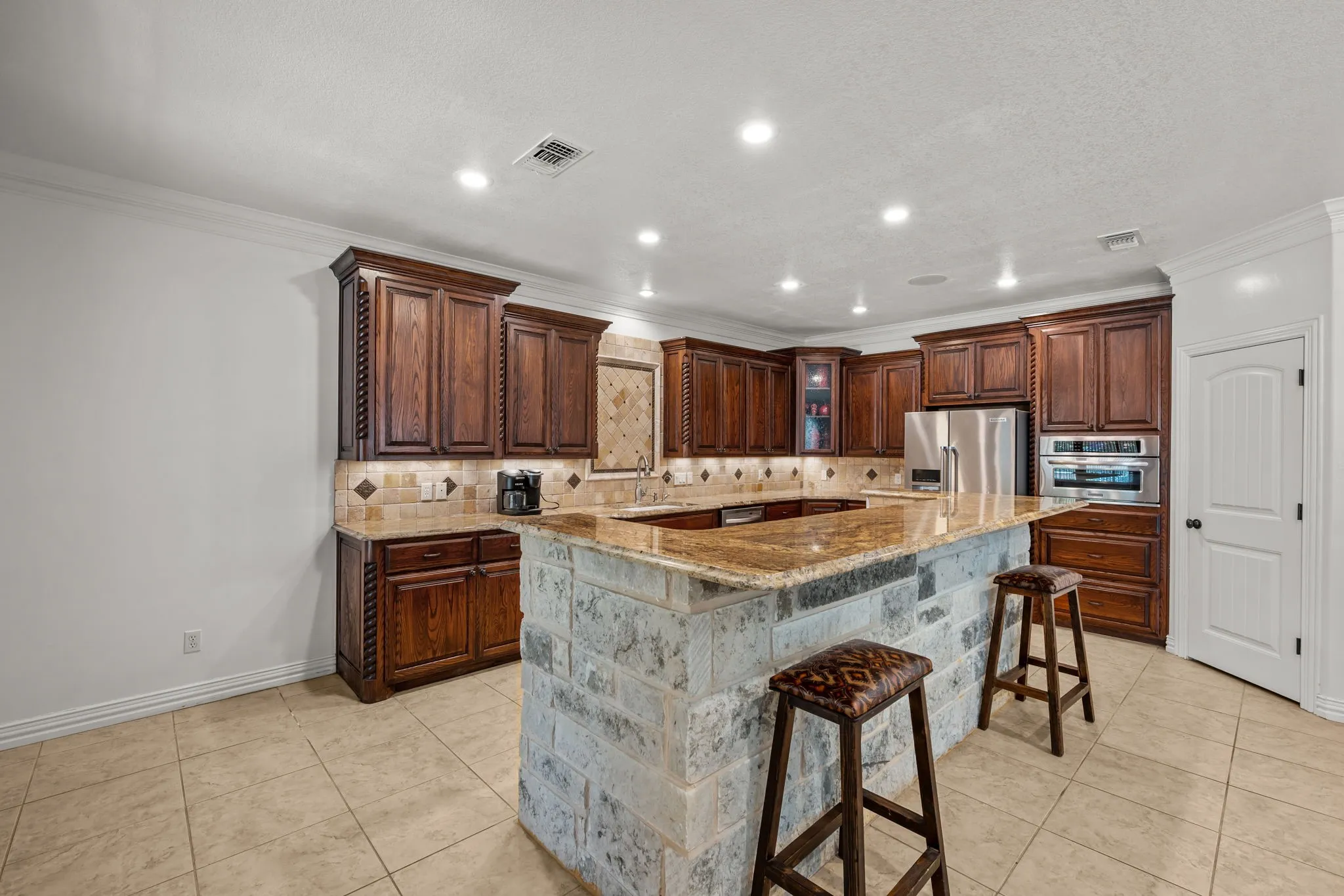 Kitchen featuring wood cabinetry, stone countertops, a stone-clad island, tile flooring, and recessed lighting