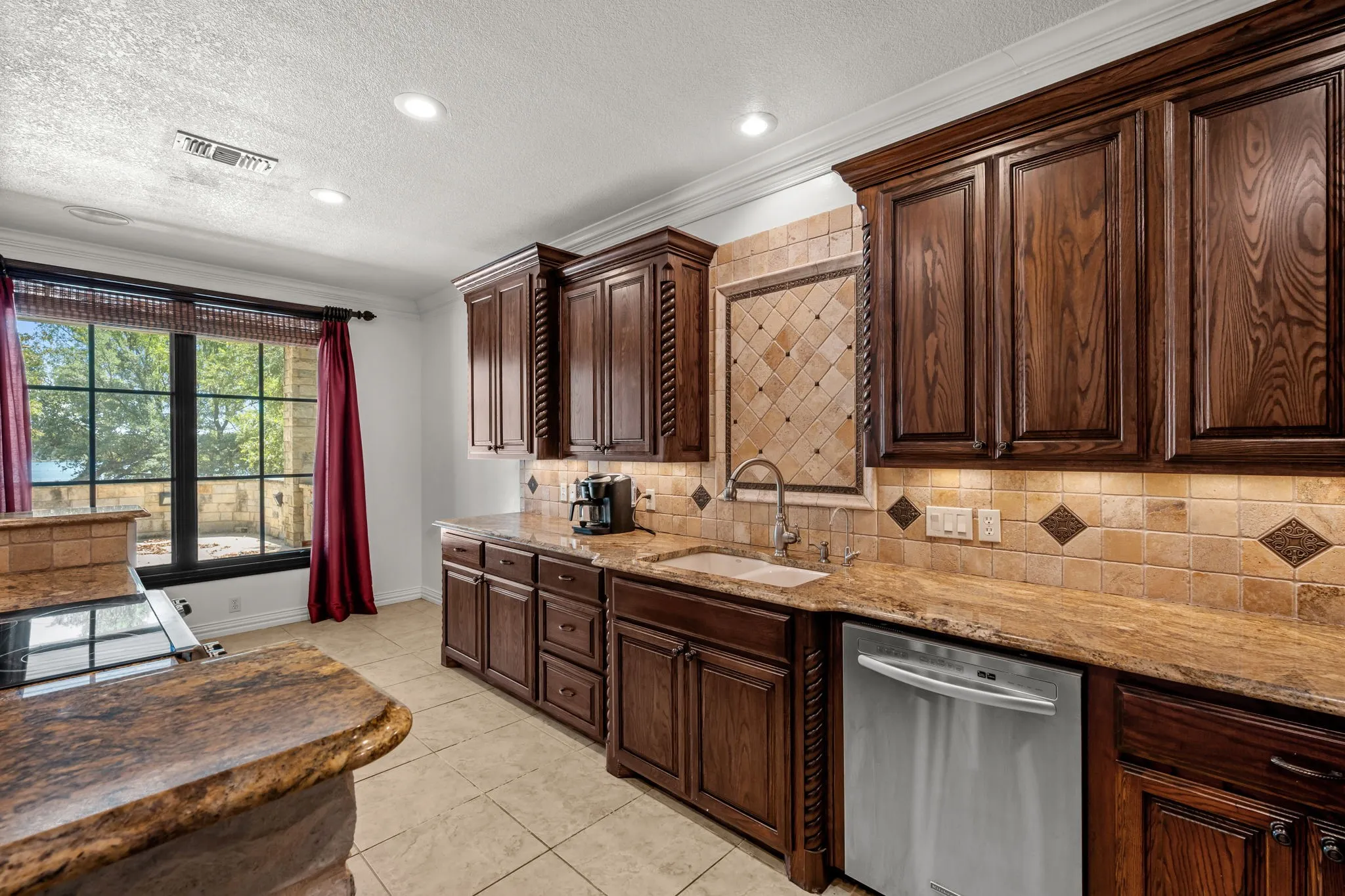 Kitchen featuring wood cabinetry, stone countertops, tile backsplash, and a stainless steel dishwasher