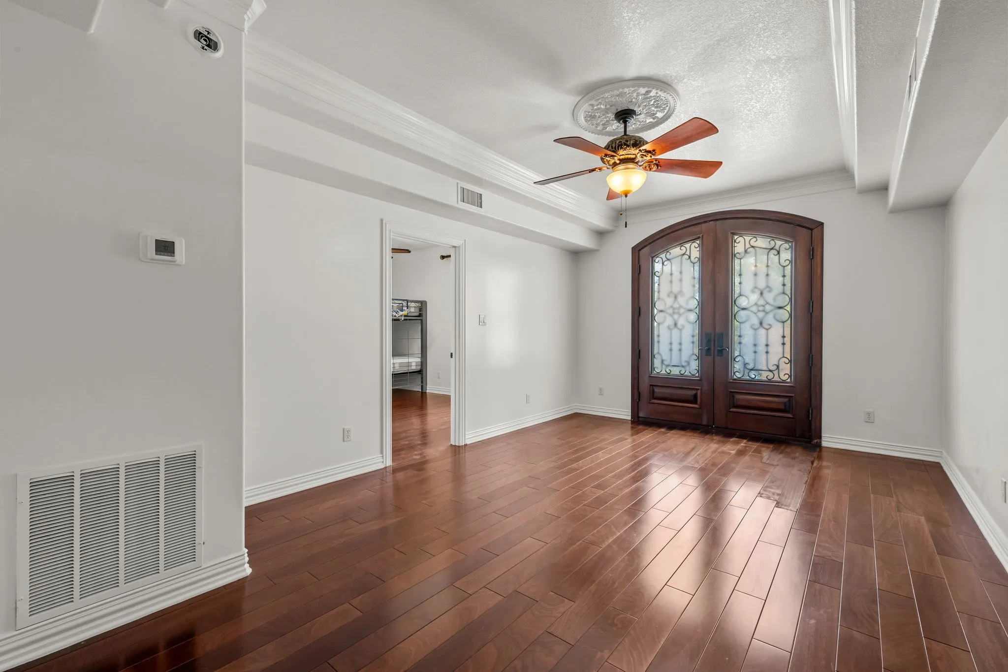 Rich wood-finish flooring, ornate double entry doors with decorative glass, and a ceiling fan with a medallion accent