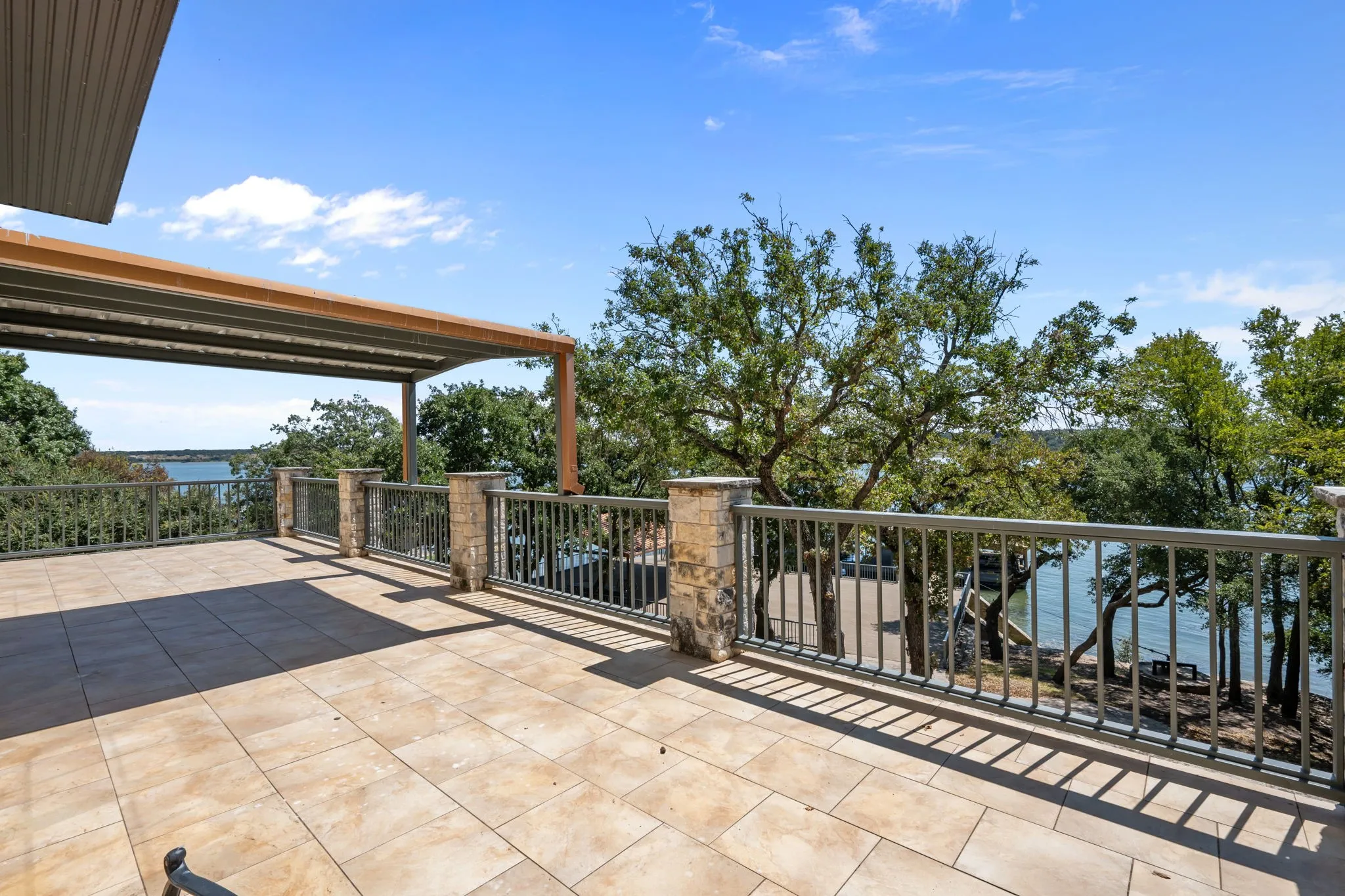 Expansive tiled patio featuring stone-clad pillars, metal railings, and a covered pergola