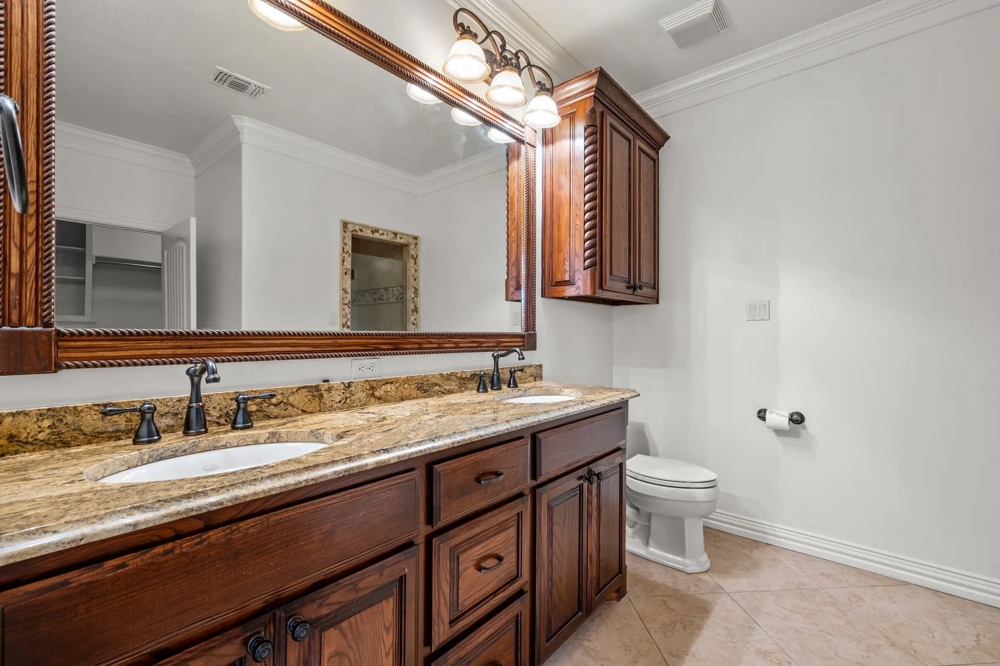 Dual undermount sinks with oil-rubbed bronze fixtures, a spacious vanity with wood-finish cabinetry, a coordinating wall-mounted storage cabinet, and crown molding