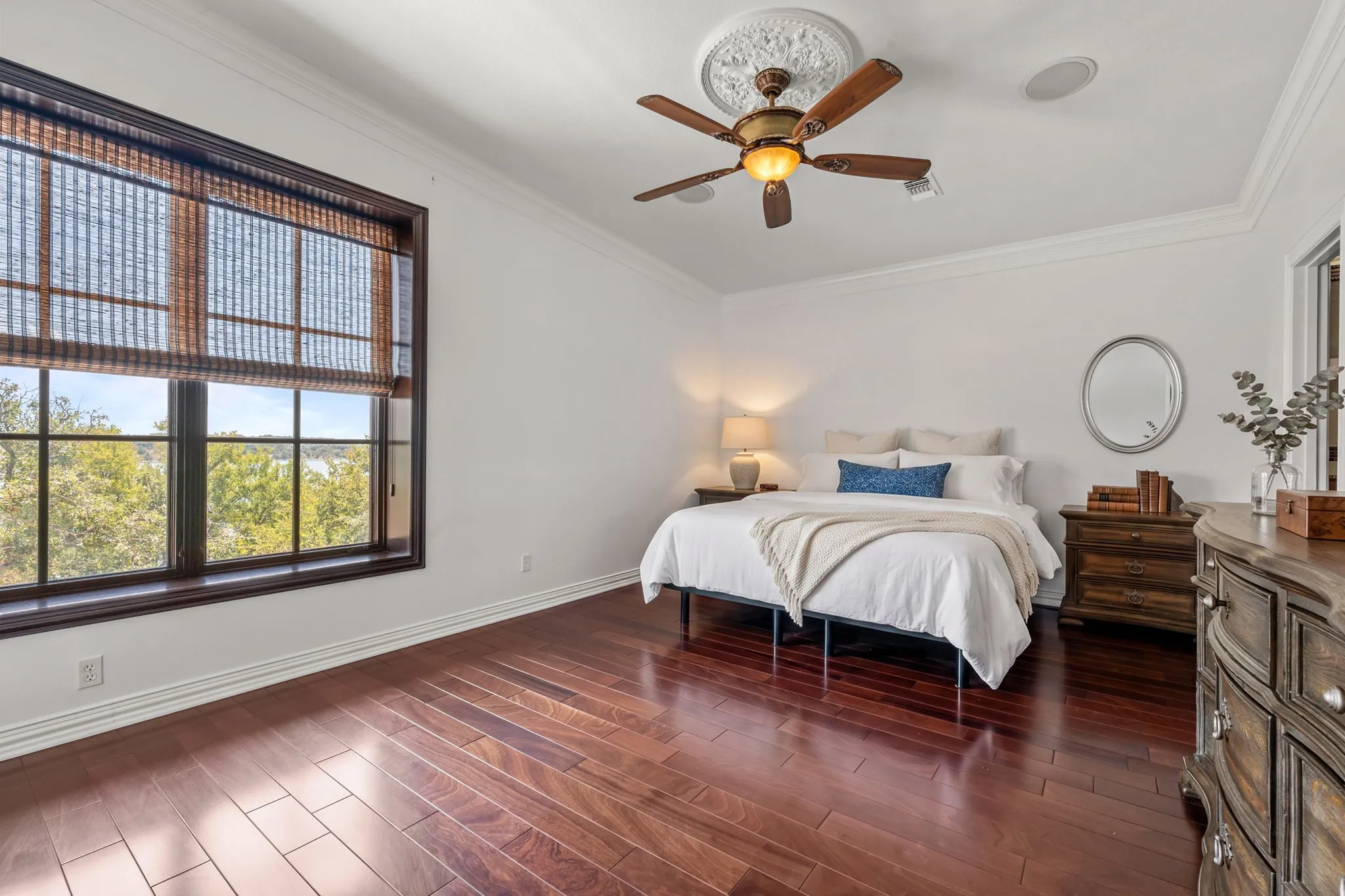 Expansive window with wood-finish framing, wood-finish flooring, ceiling fan with ornate medallion, crown molding, and recessed ceiling speakers-Staged
