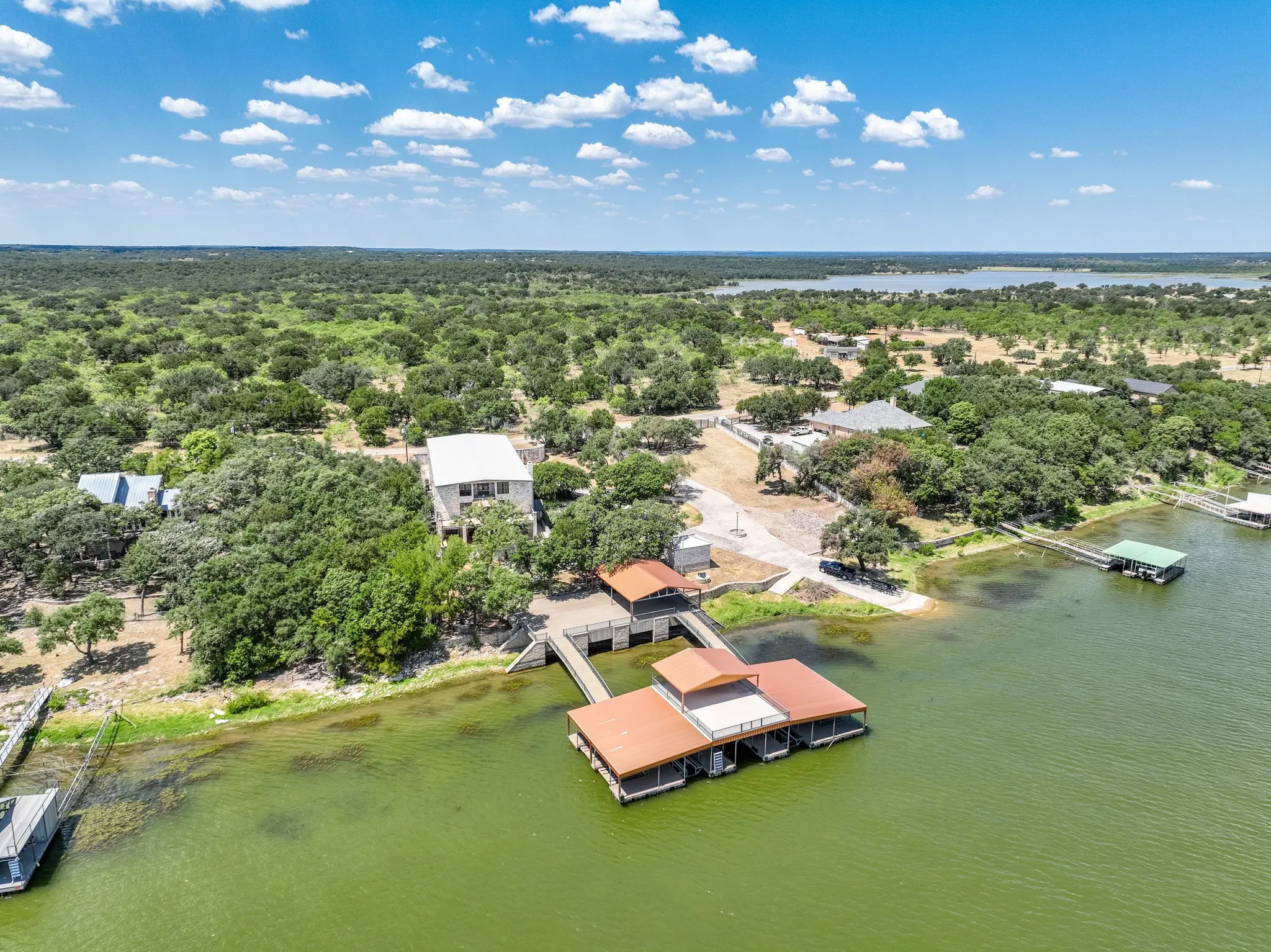 Waterfront property featuring a private boat dock with multiple slips, a covered boat lift, a private boat ramp, and a multi-level residence surrounded by mature trees