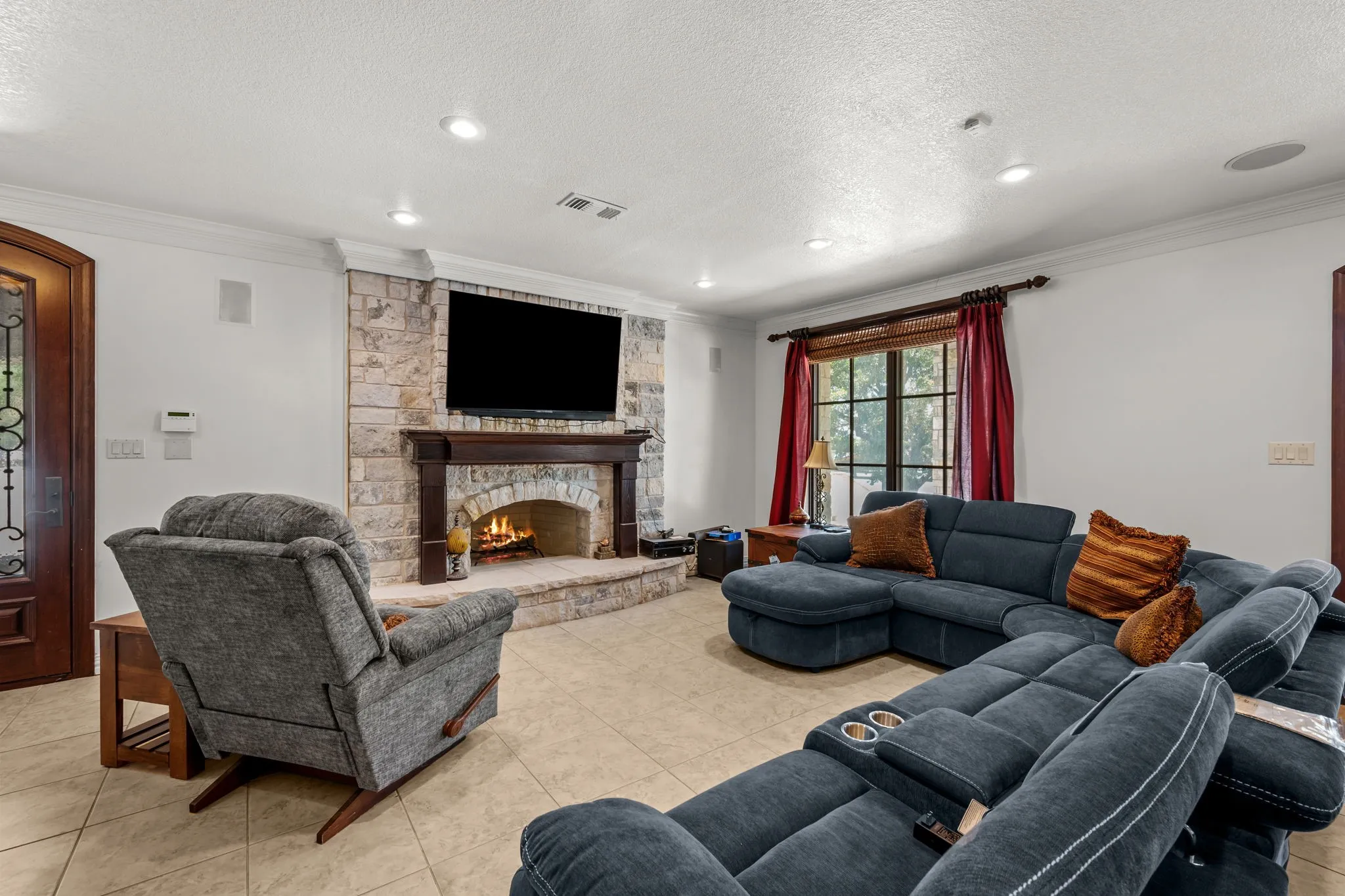Stone-faced fireplace with wood mantel, large window with transom, tile flooring, built-in ceiling speakers, and recessed lighting