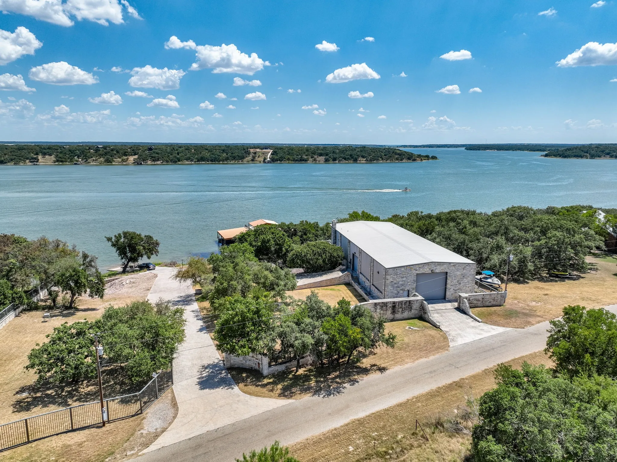 Waterfront property featuring a private boat dock, a stone-clad industrial-style building with a metal roof, and a paved driveway