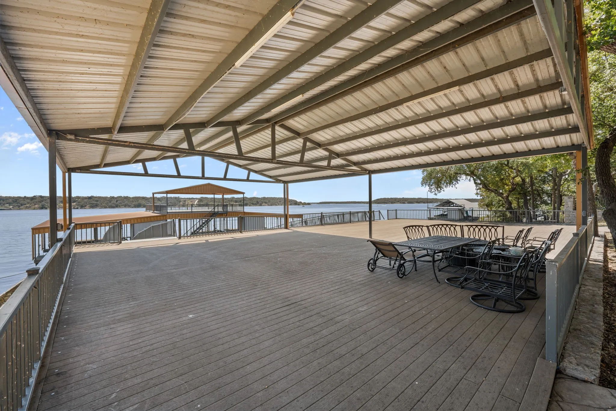 Expansive covered patio with composite decking and metal railings, overlooking a multi-level boat dock with a covered slip and lake access