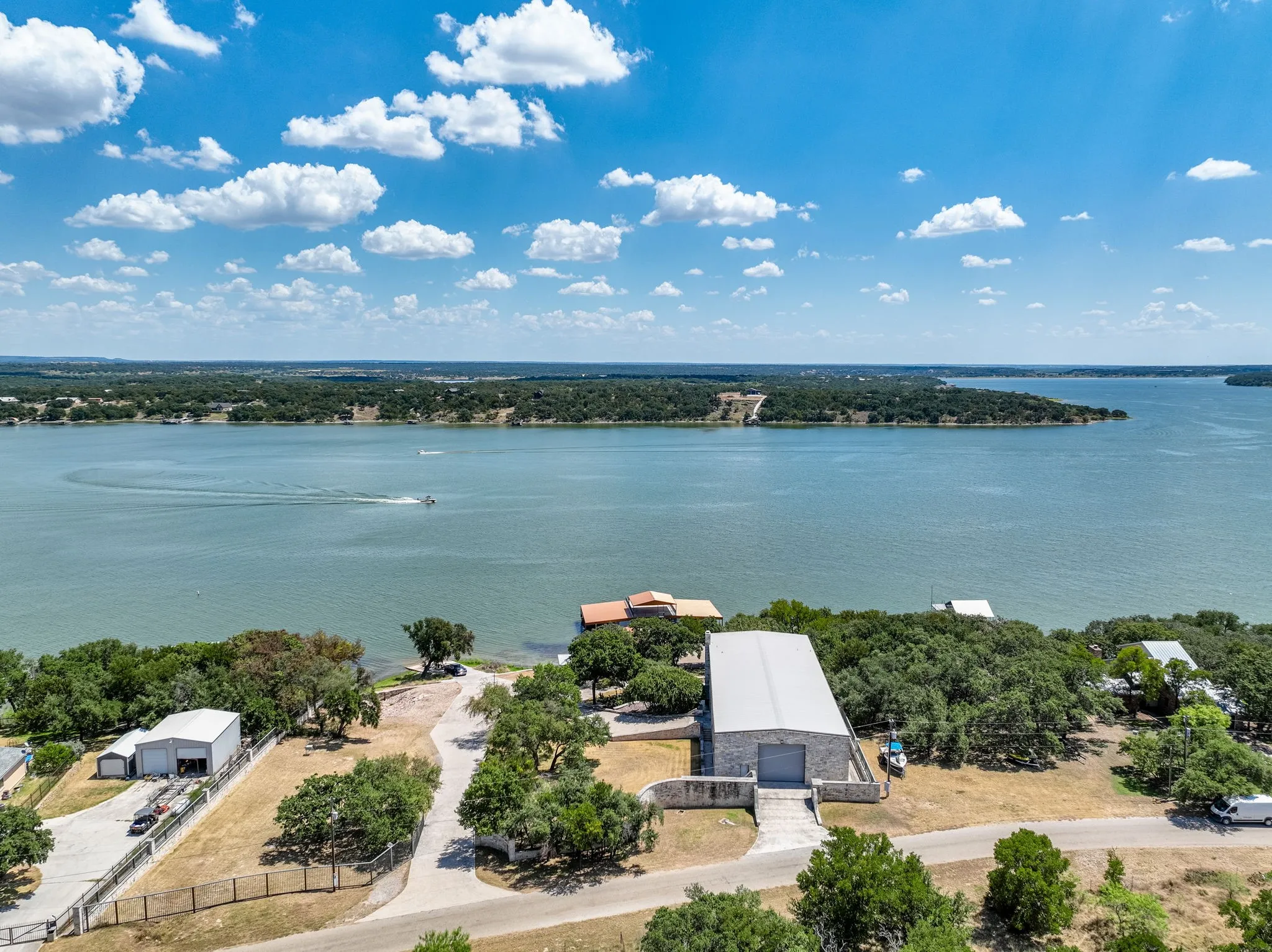 Expansive waterfront property featuring a large metal-roofed structure, additional outbuilding, mature trees, and direct water access