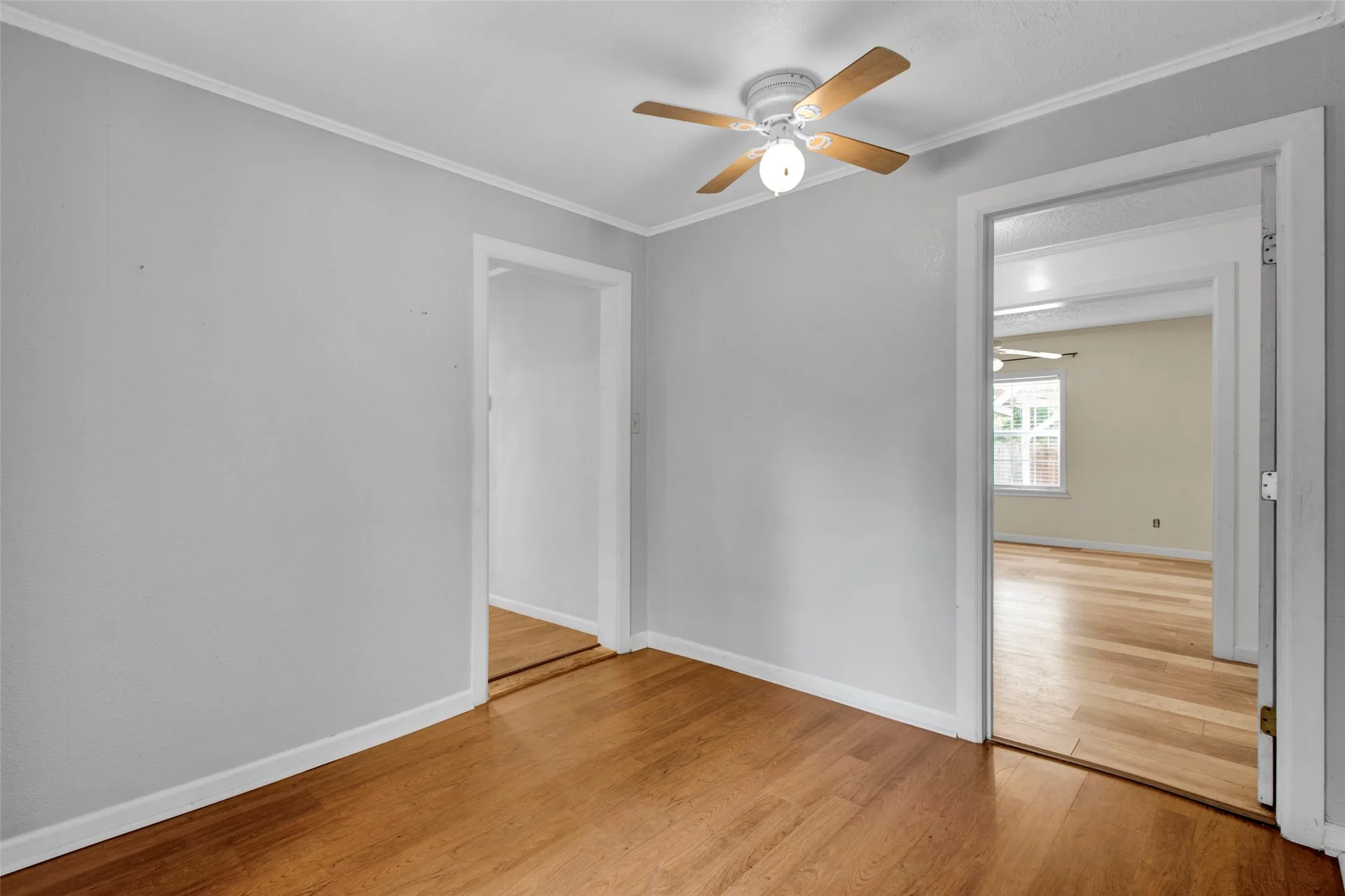 Hardwood-finish flooring throughout, light gray wall paint, and a ceiling fan with integrated lighting