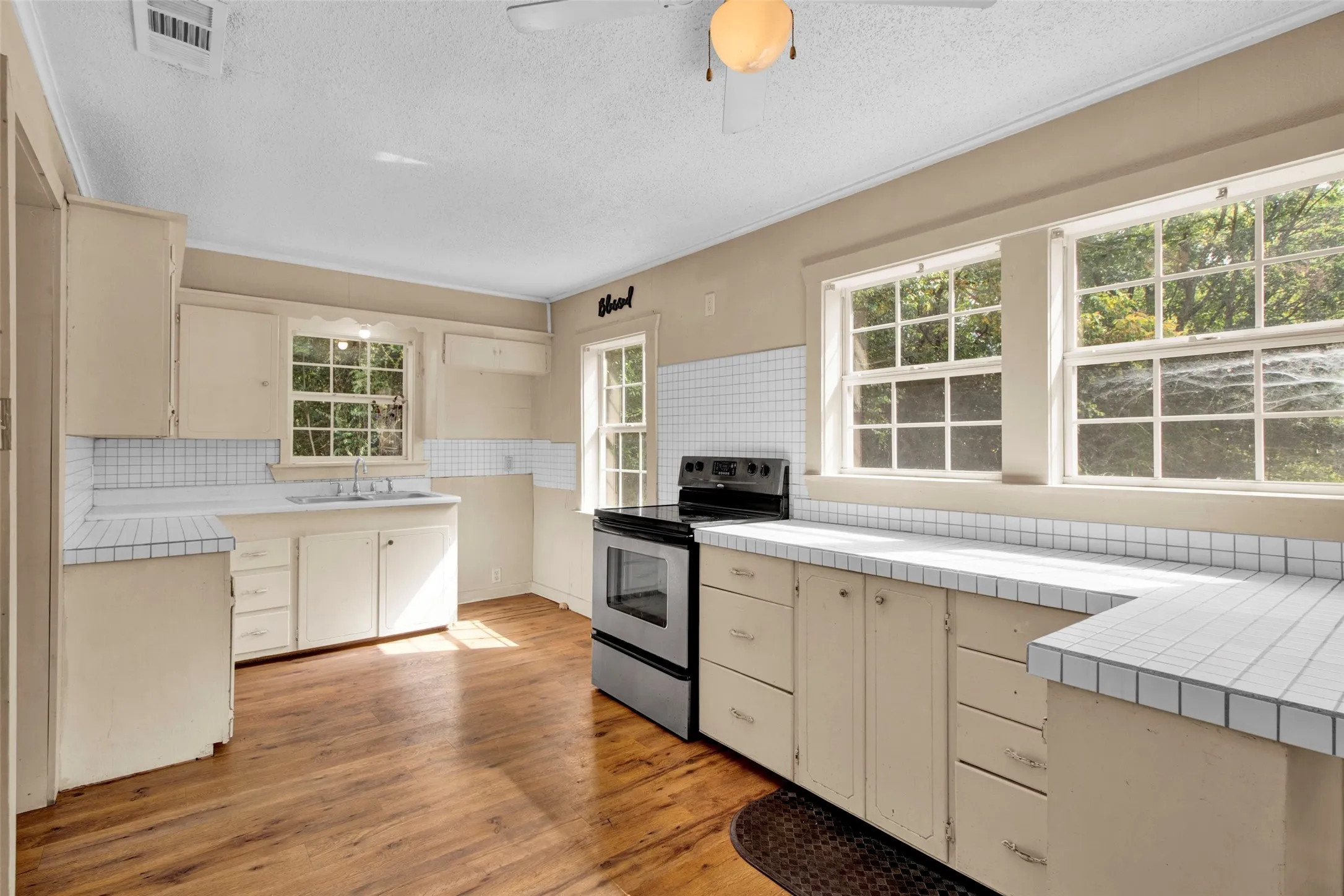 Kitchen featuring wood-finish flooring, white tile countertops, white tile backsplash, light-toned cabinetry, and multiple windows