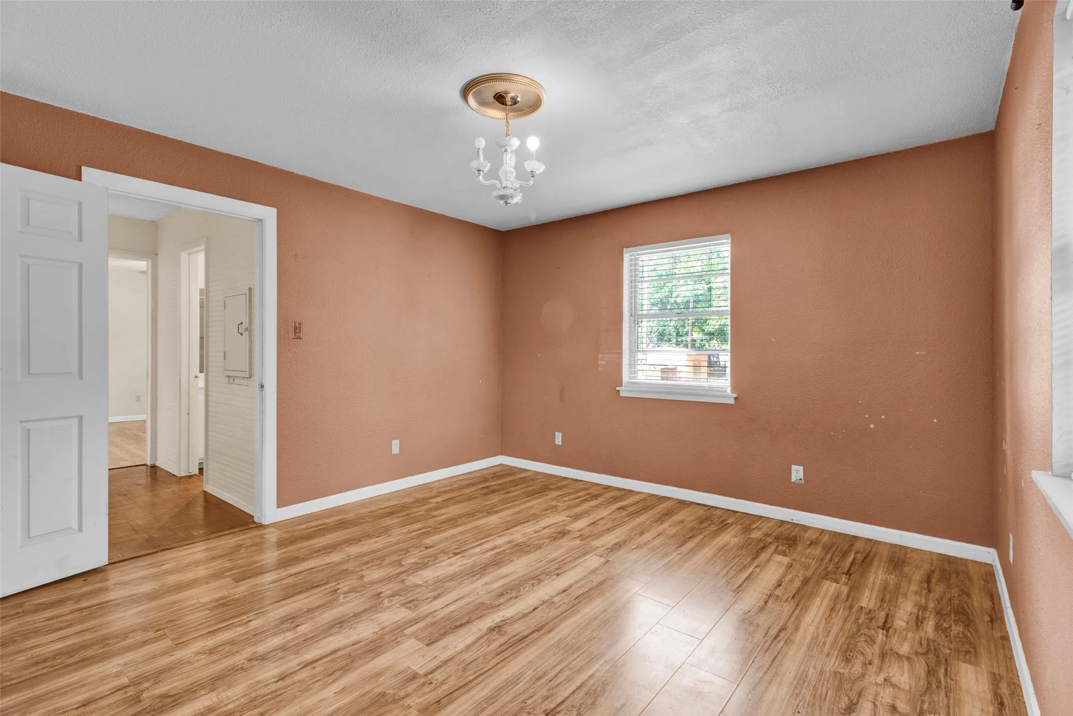 Wood-finish flooring, single window with blinds, white trim throughout, and a decorative ceiling light fixture