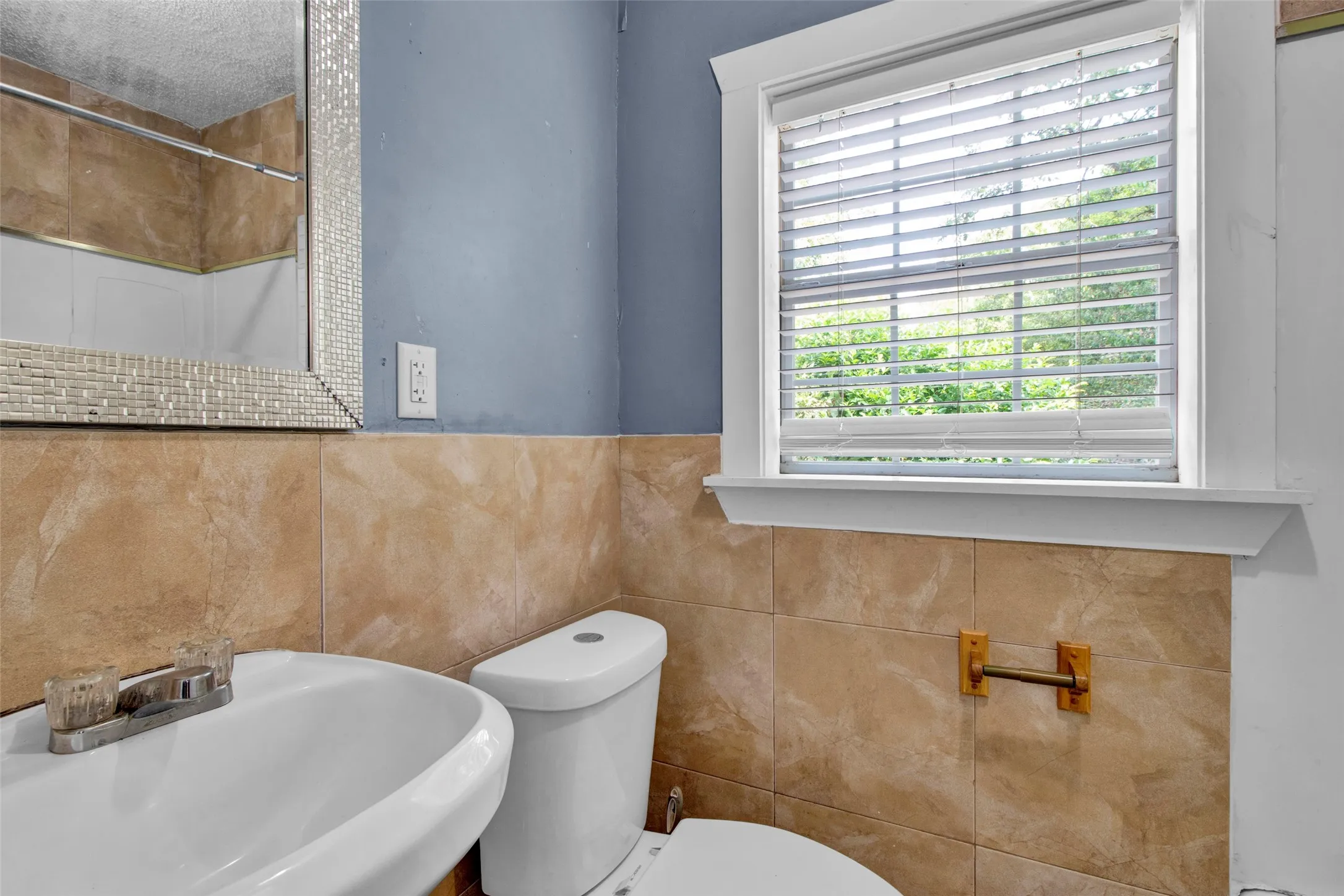 Bathroom featuring a pedestal sink, toilet, and a window with blinds