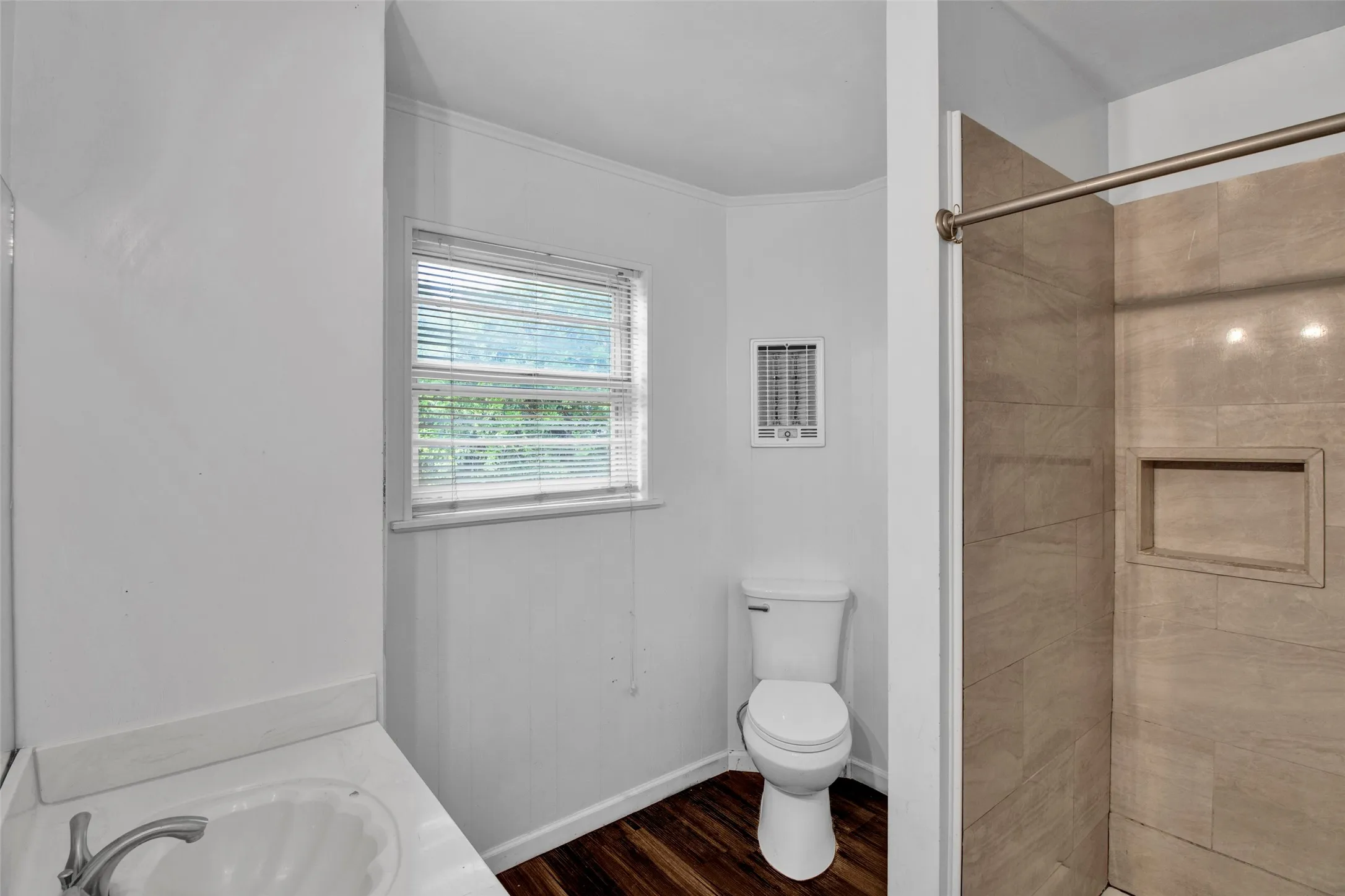 Bathroom featuring a vanity with an integrated sink, a window with blinds, wood-finish flooring, a toilet, and a tiled shower with a recessed niche