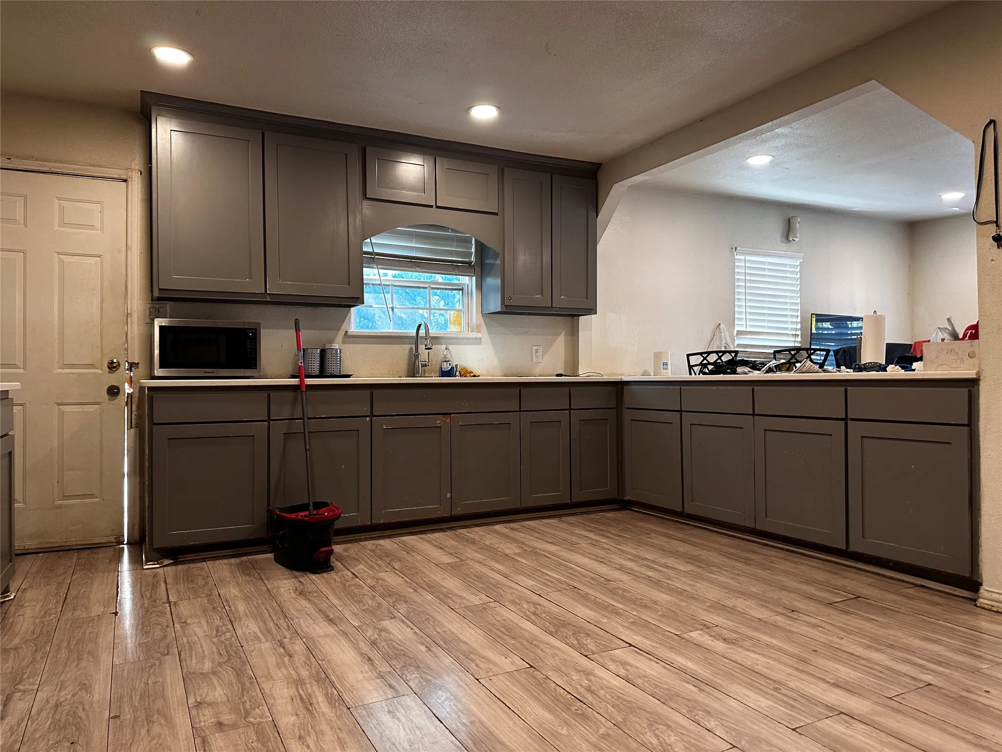 Wood-finish flooring, recessed lighting, gray shaker-style cabinetry, and light-toned countertops