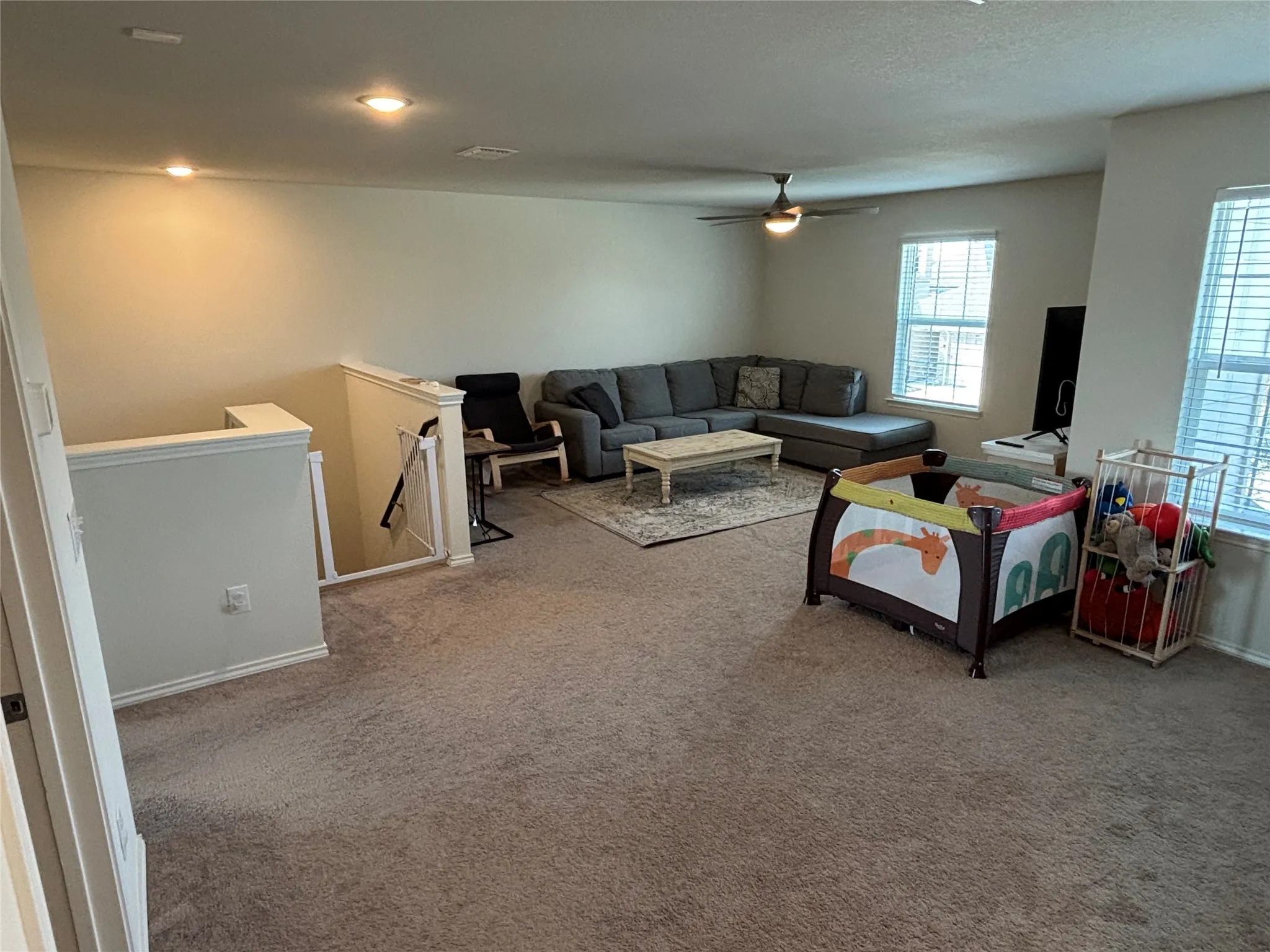 Spacious carpeted area with recessed lighting, ceiling fan, and two windows with blinds