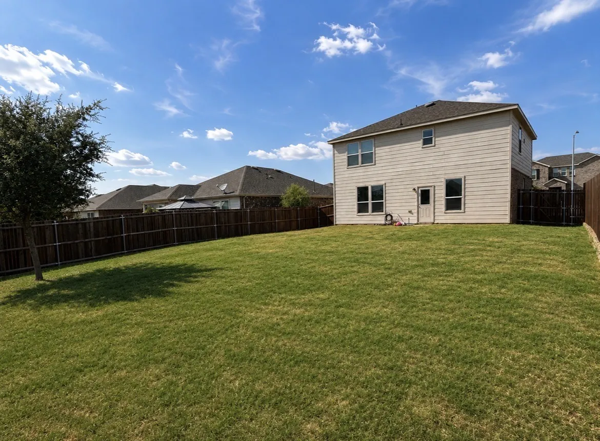 Expansive backyard featuring a manicured lawn, a full privacy fence, and mature landscaping