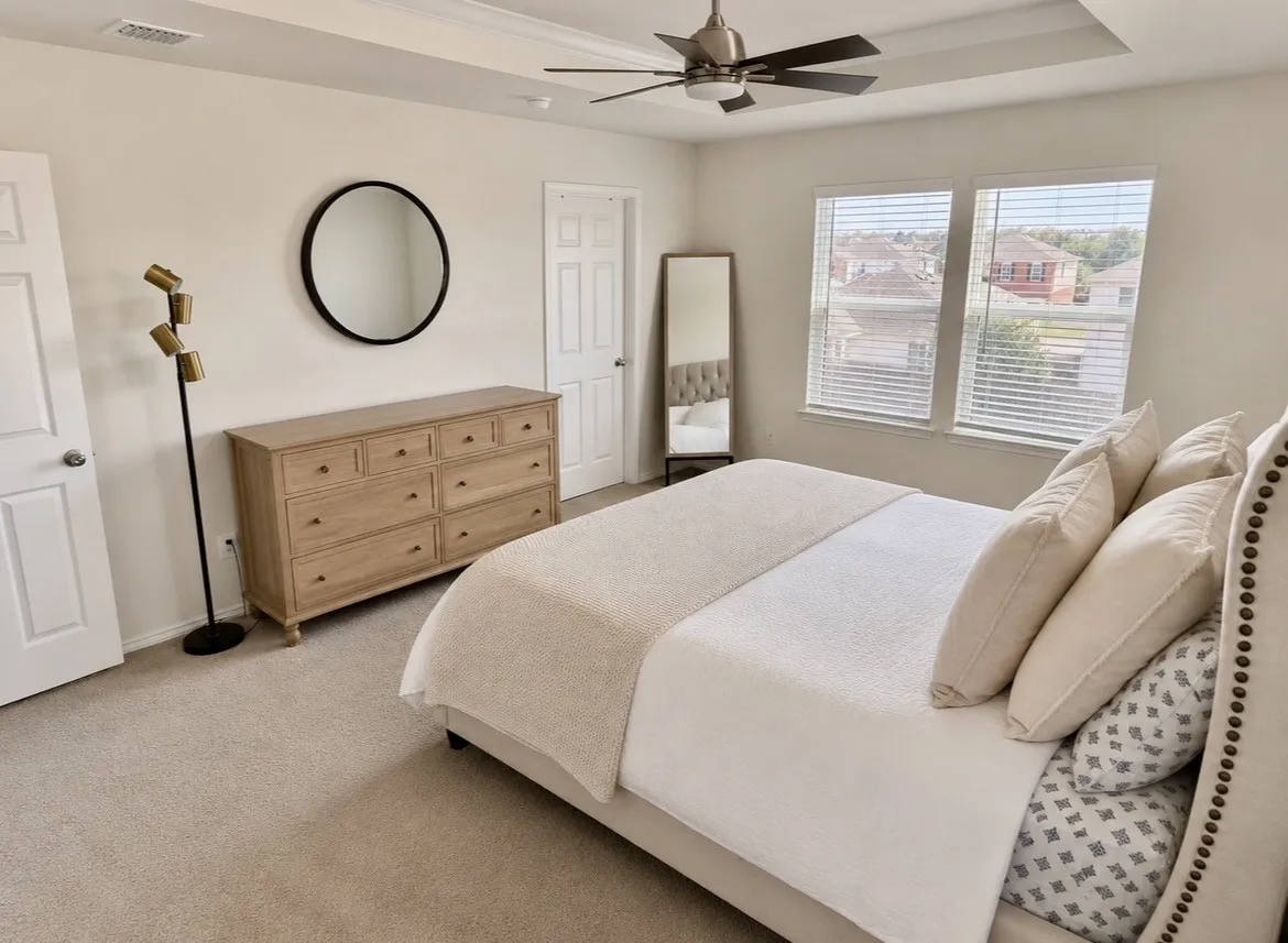 Tray ceiling with a ceiling fan, two windows with horizontal blinds, neutral wall paint, and light-toned carpeting