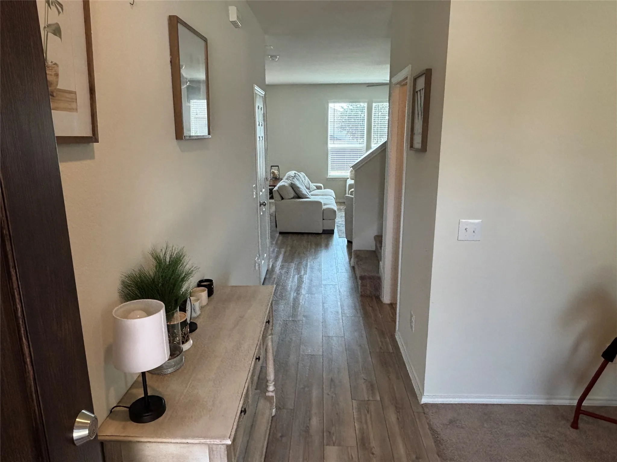Wood-finish flooring extending through a hallway, white painted walls, and a staircase with carpeted treads