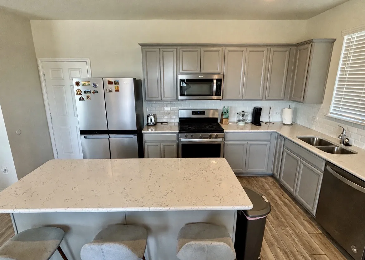 Kitchen featuring a central island with countertop seating, light-toned countertops, gray cabinetry, stainless steel appliances, and a subway tile backsplash