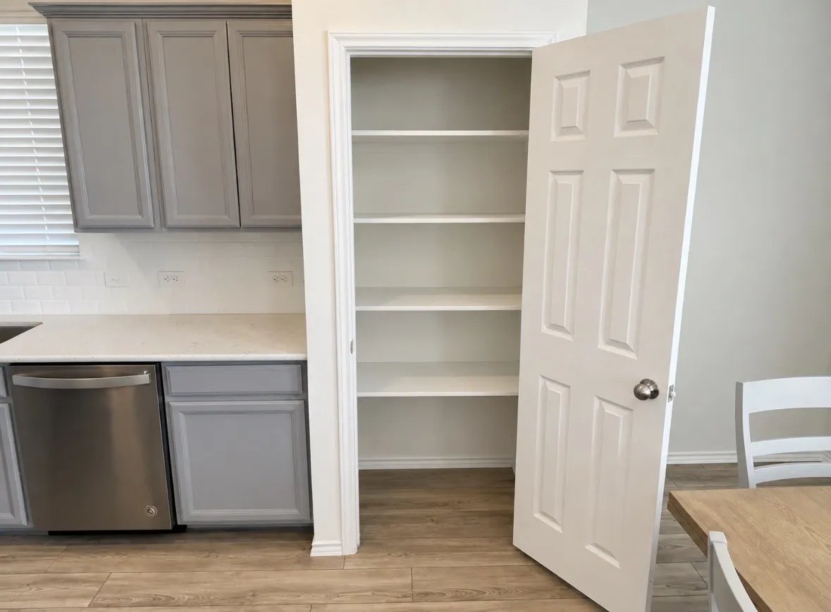 Kitchen featuring gray cabinetry, light-toned countertops, a stainless steel dishwasher, white subway tile backsplash, and wood-finish flooring