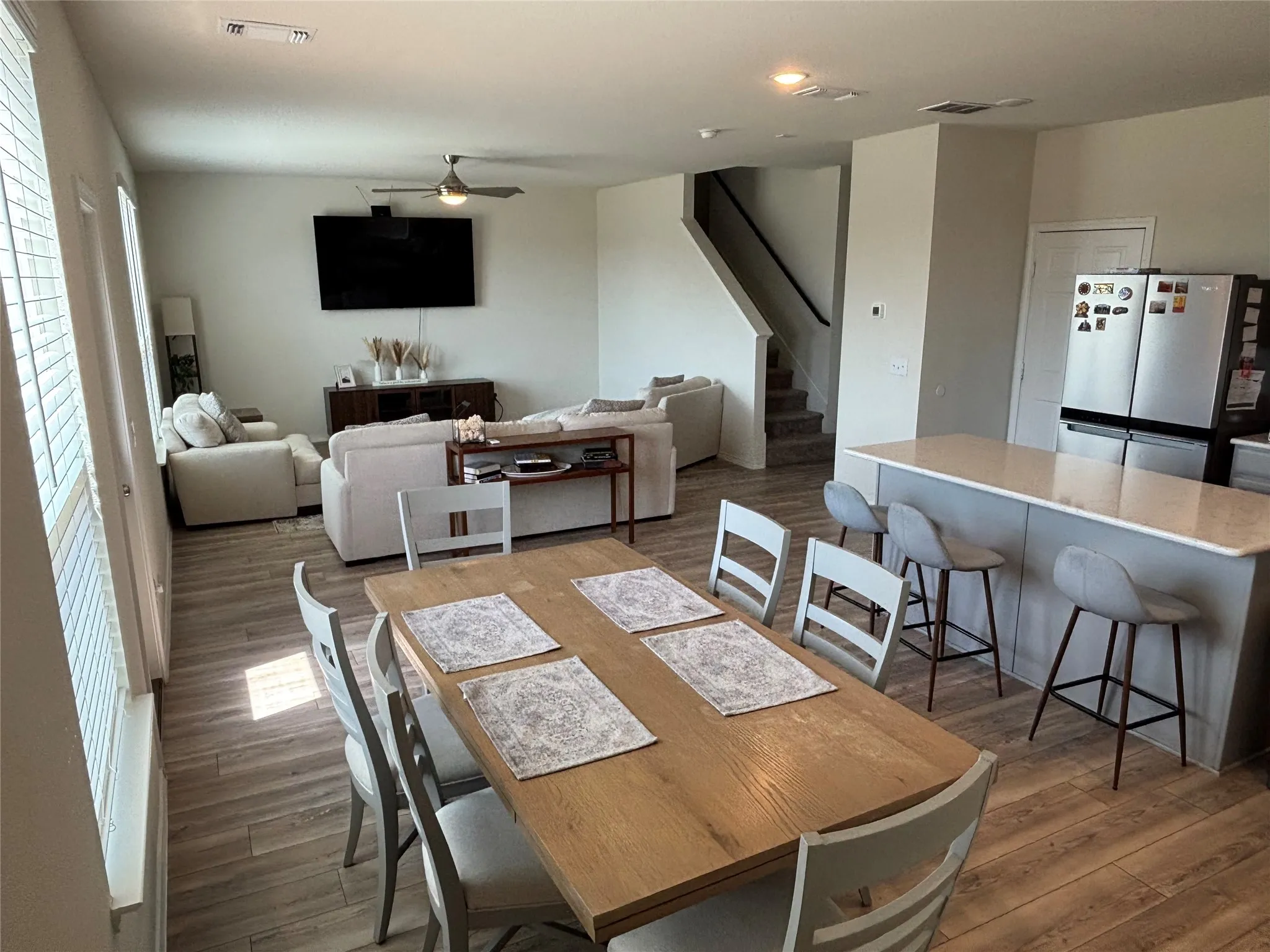 Open-concept living space with wood-finish flooring, a kitchen island with seating, and a staircase featuring carpeted treads