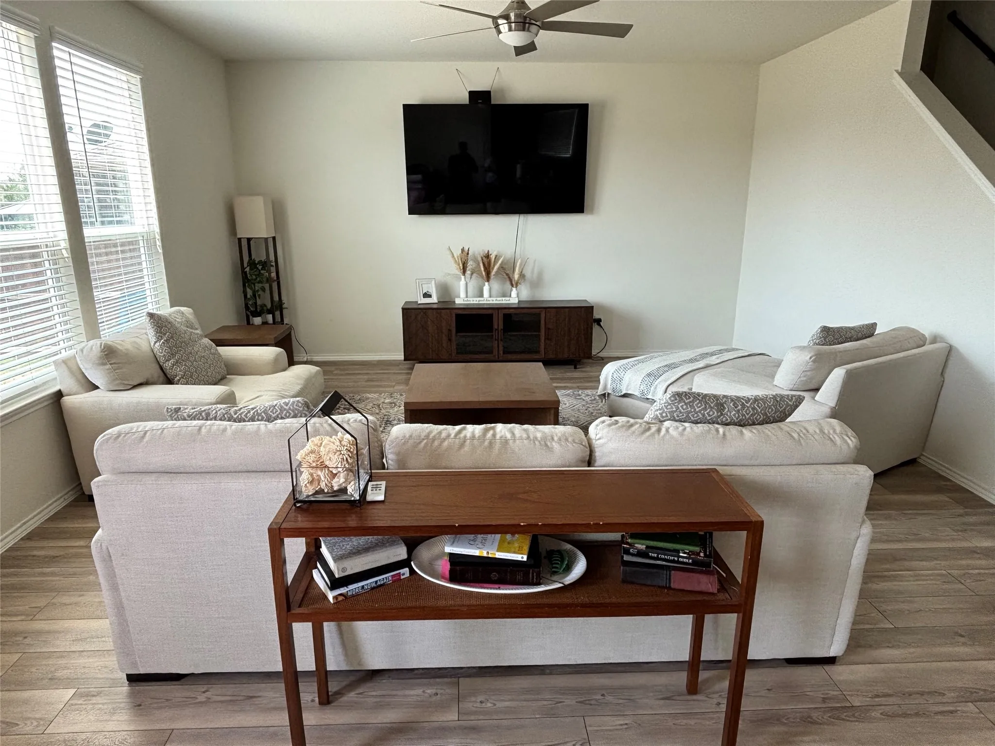 Living area featuring wood-finish flooring, a ceiling fan with integrated lighting, and multiple windows with blinds