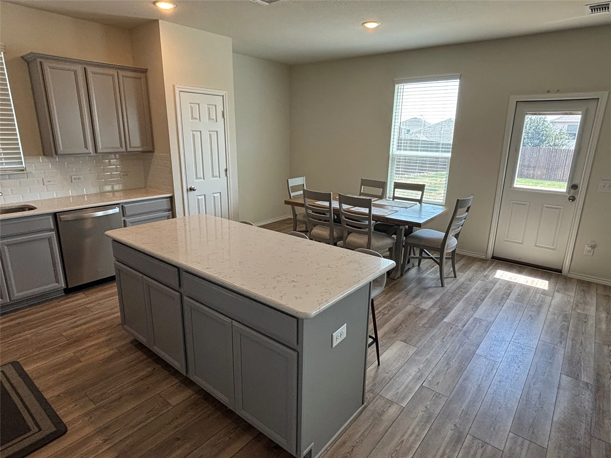 Kitchen featuring a central island with a light-colored countertop, grey cabinetry, stainless steel dishwasher, and a white subway tile backsplash