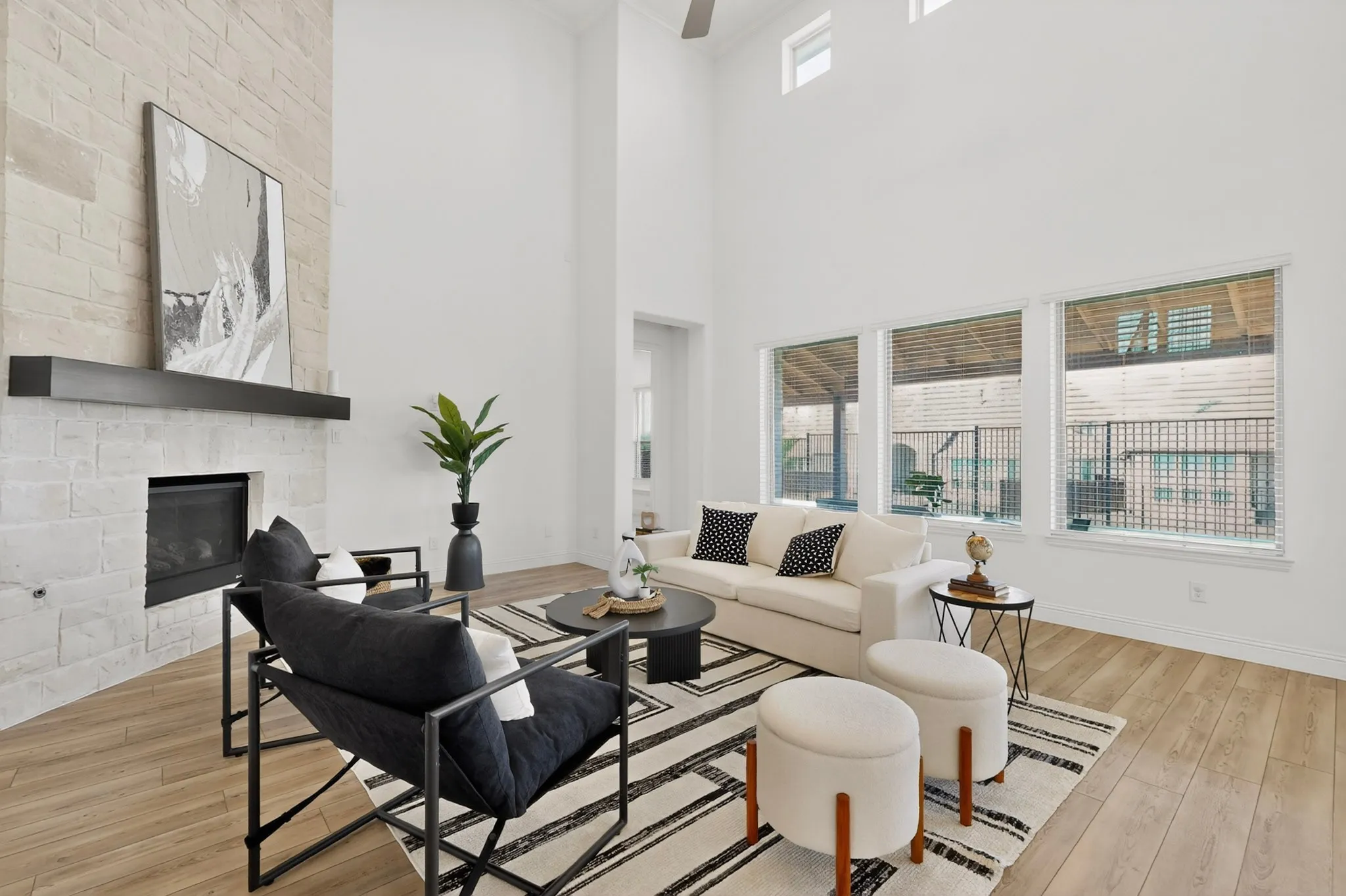 Two-story living area featuring a stone fireplace with a dark wood mantel, high ceilings, wood-finish flooring, and multiple large windows