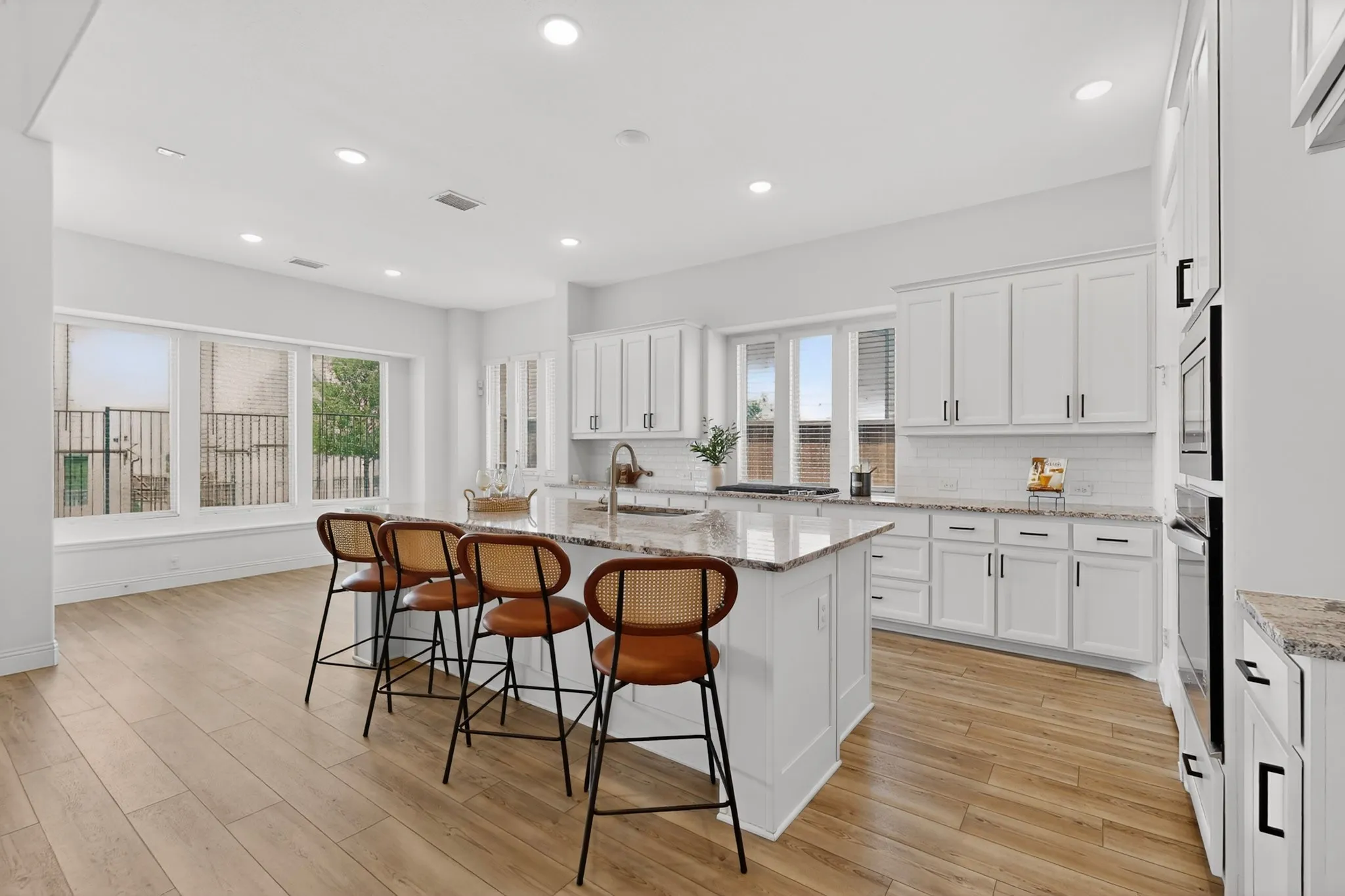 Kitchen featuring wood-finish flooring, a central island with countertop seating, white shaker-style cabinetry, granite countertops, and stainless steel appliances