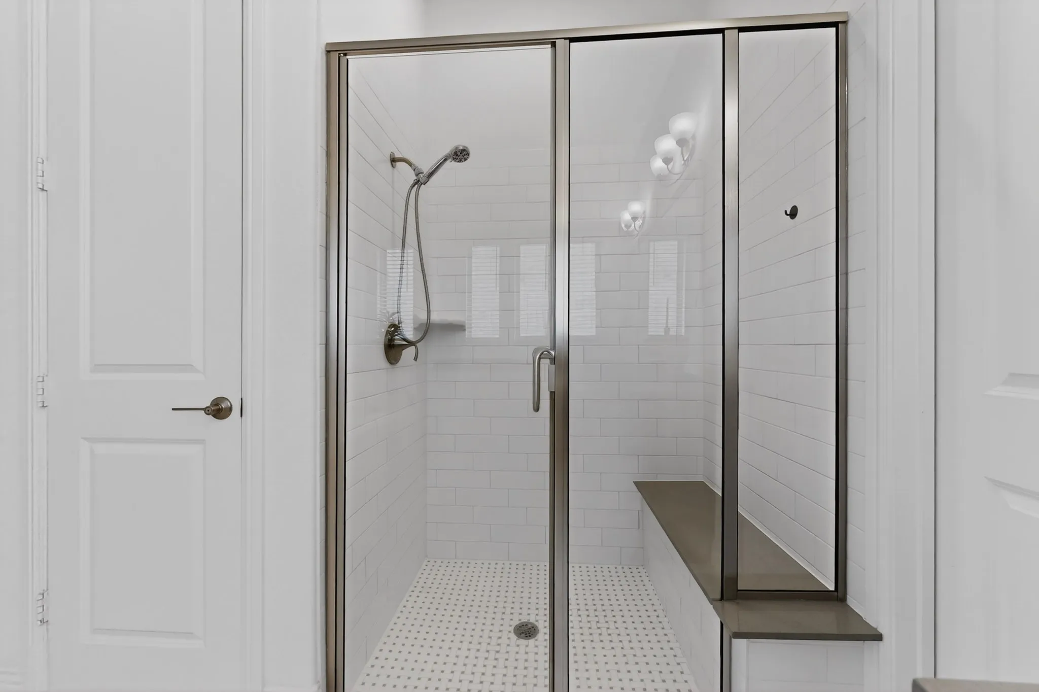 Glass-enclosed shower with white subway tile, a built-in shower bench, and a handheld shower head