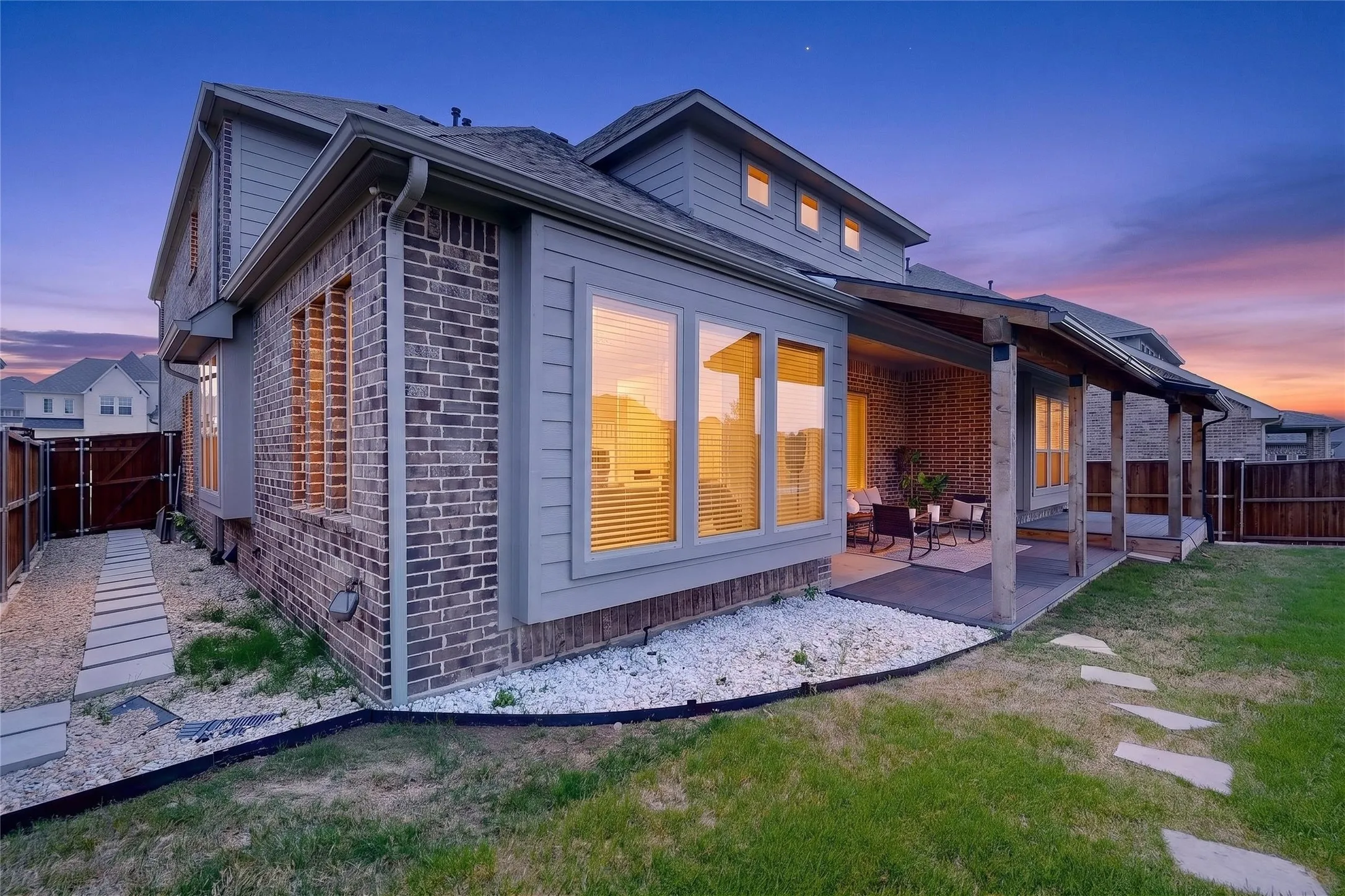 Brick and siding exterior, large windows, covered patio with wood columns, gravel beds, and a stepping stone pathway