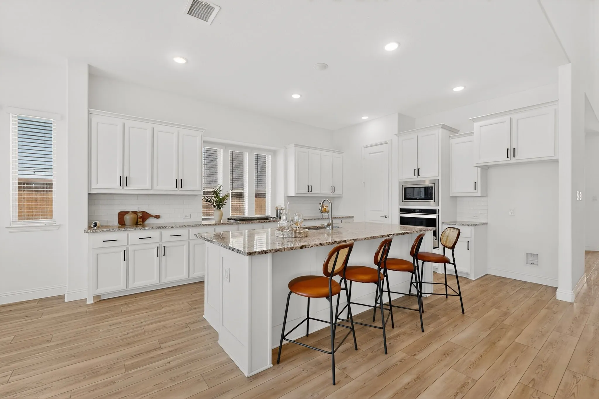 Kitchen featuring wood-finish flooring, white cabinetry, granite countertops, and a center island with bar seating